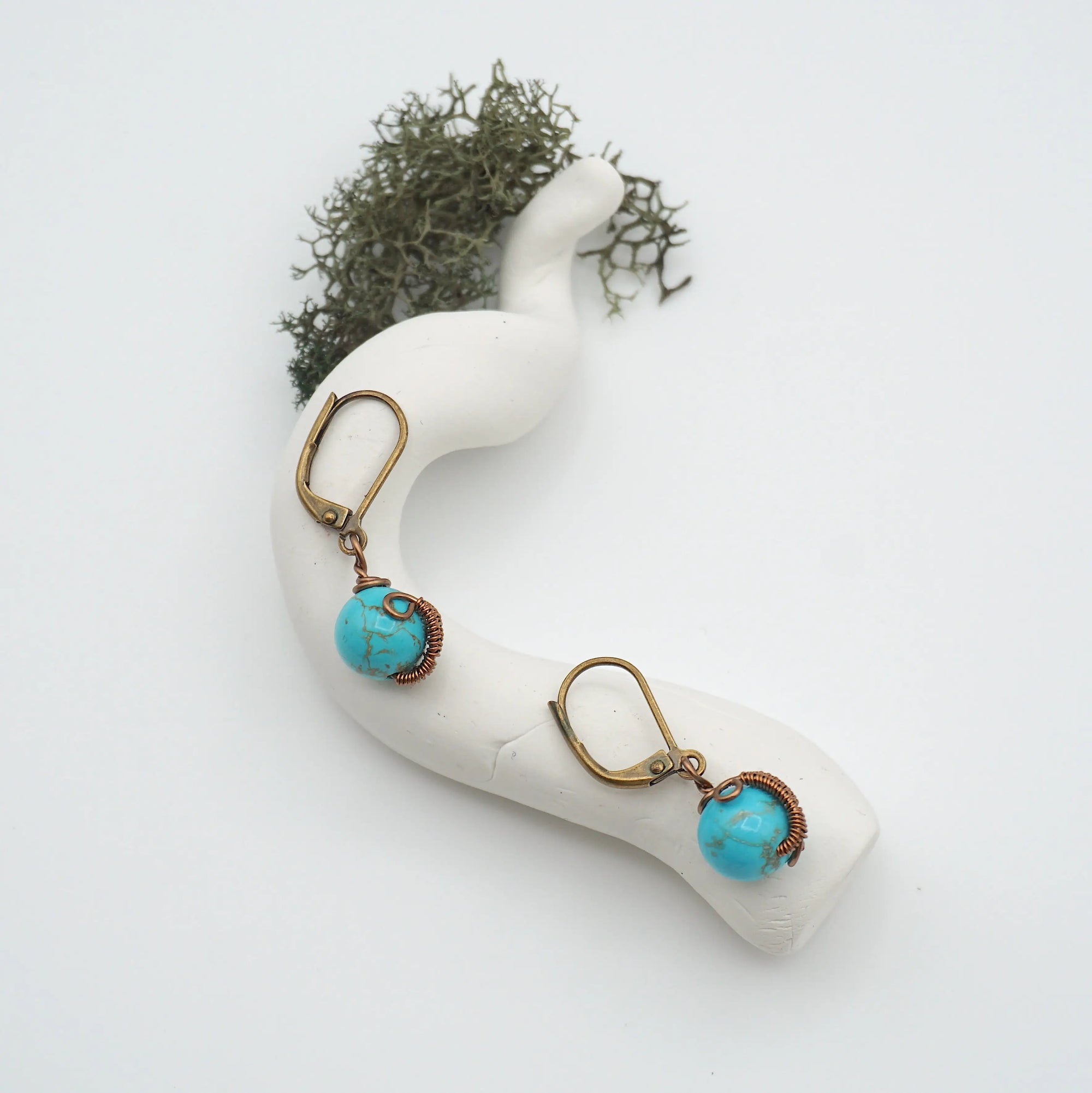 Bird’s eye view of turquoise drop earrings laying flat on a display, showing detailed wire wrapping and gemstone color.