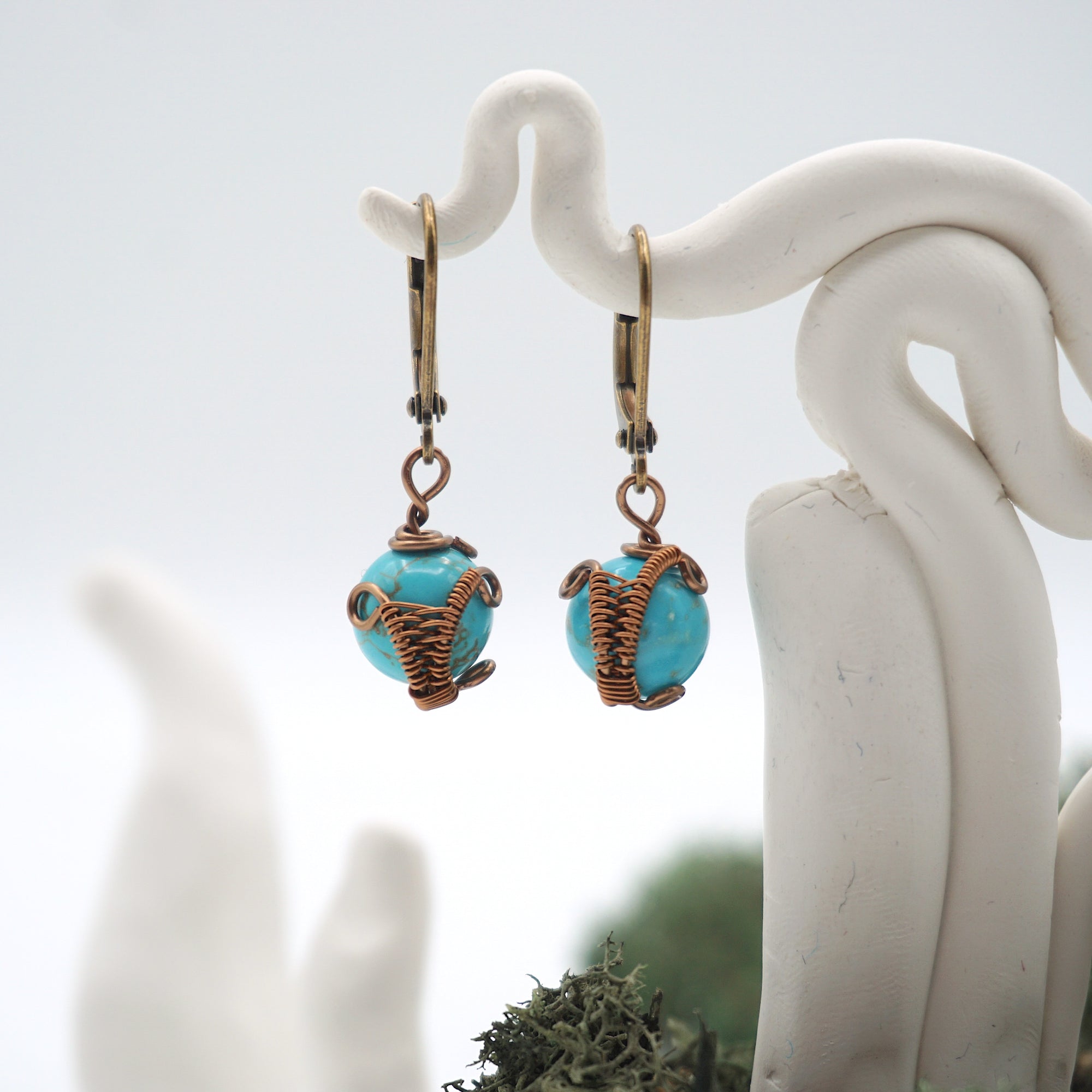 Close-up of handcrafted turquoise drop earrings with antique bronze copper wire wrapping.