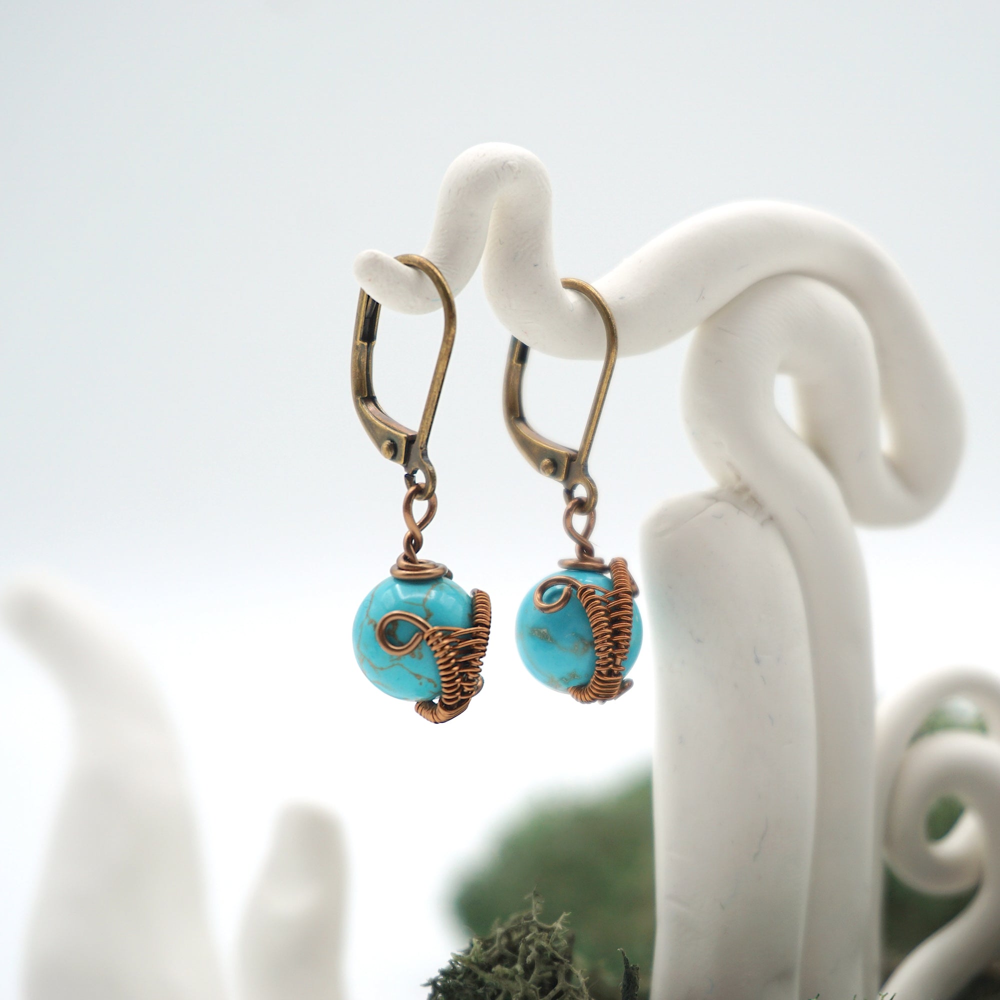 Side angle of turquoise drop earrings on a display stand, highlighting antique bronze copper wire wrapping.