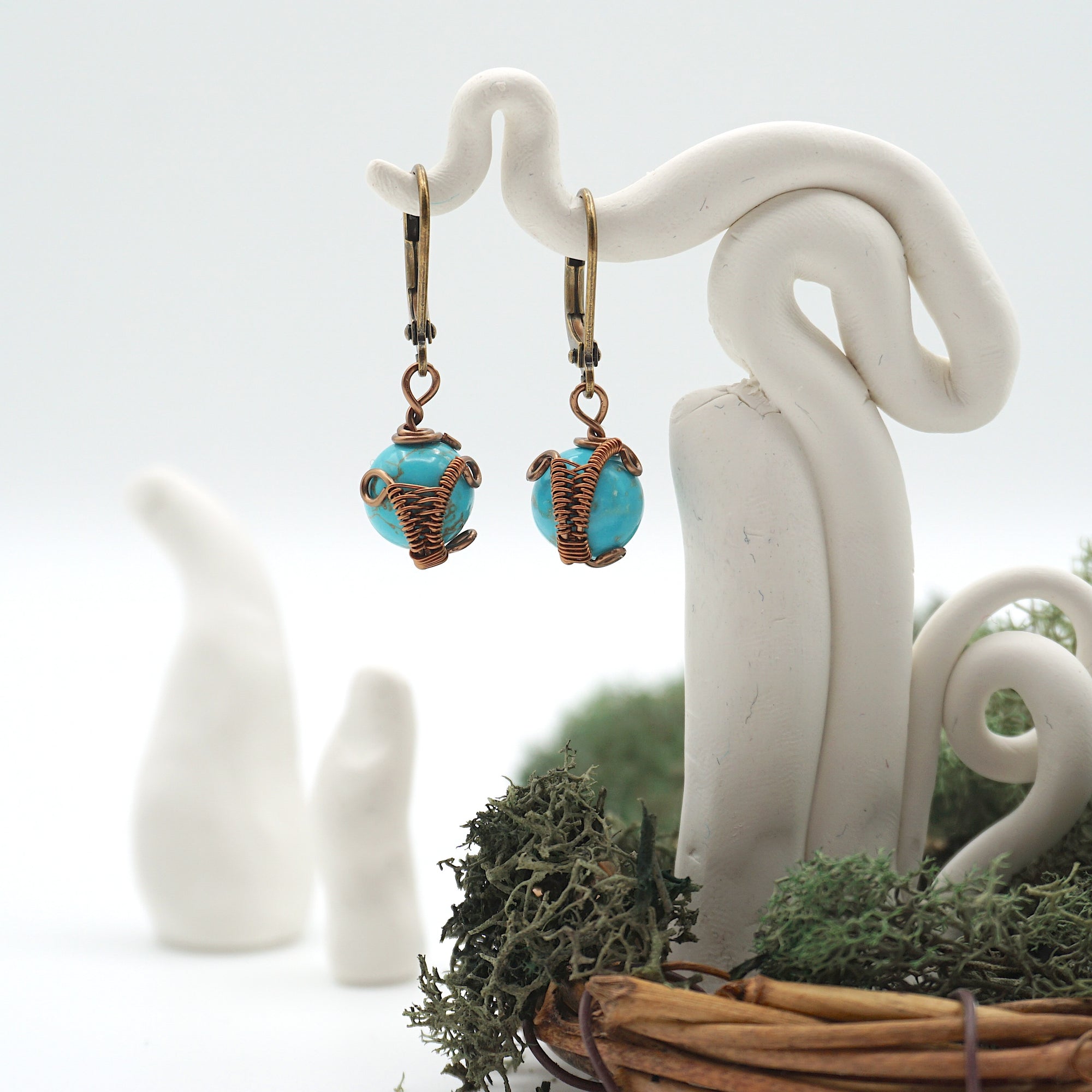 Front angle of turquoise drop earrings hanging on a jewelry display, wire-wrapped design.