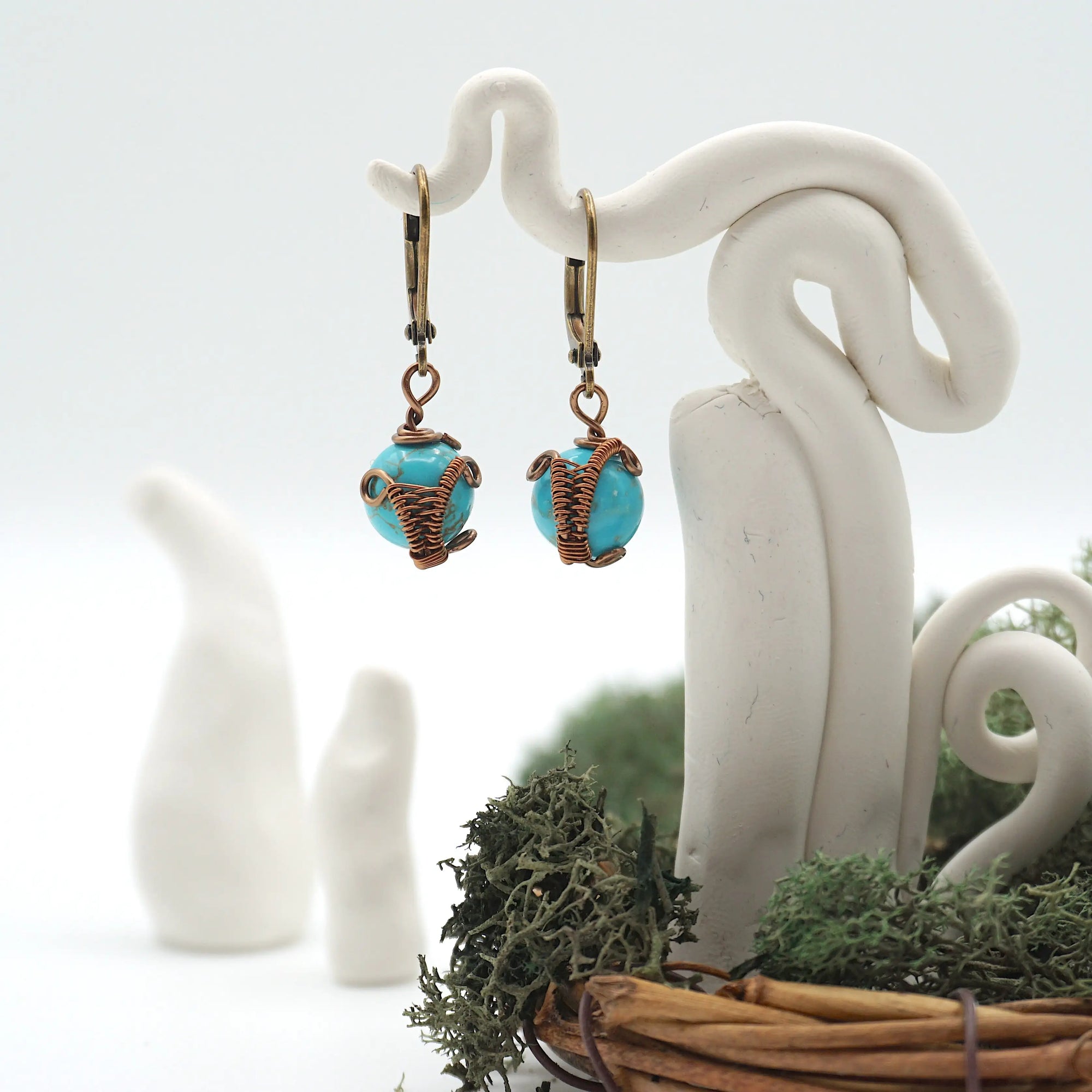 Front angle of turquoise drop earrings hanging on a jewelry display, wire-wrapped design.