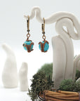 Front angle of turquoise drop earrings hanging on a jewelry display, wire-wrapped design.