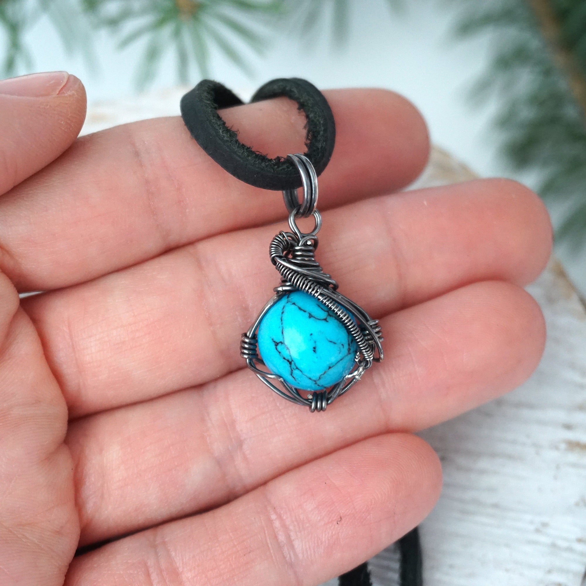 Turquoise pendant for men in hand showing size with sterling silver wire wrap black cord