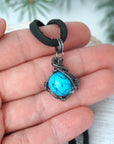 Turquoise pendant for men in hand showing size with sterling silver wire wrap black cord