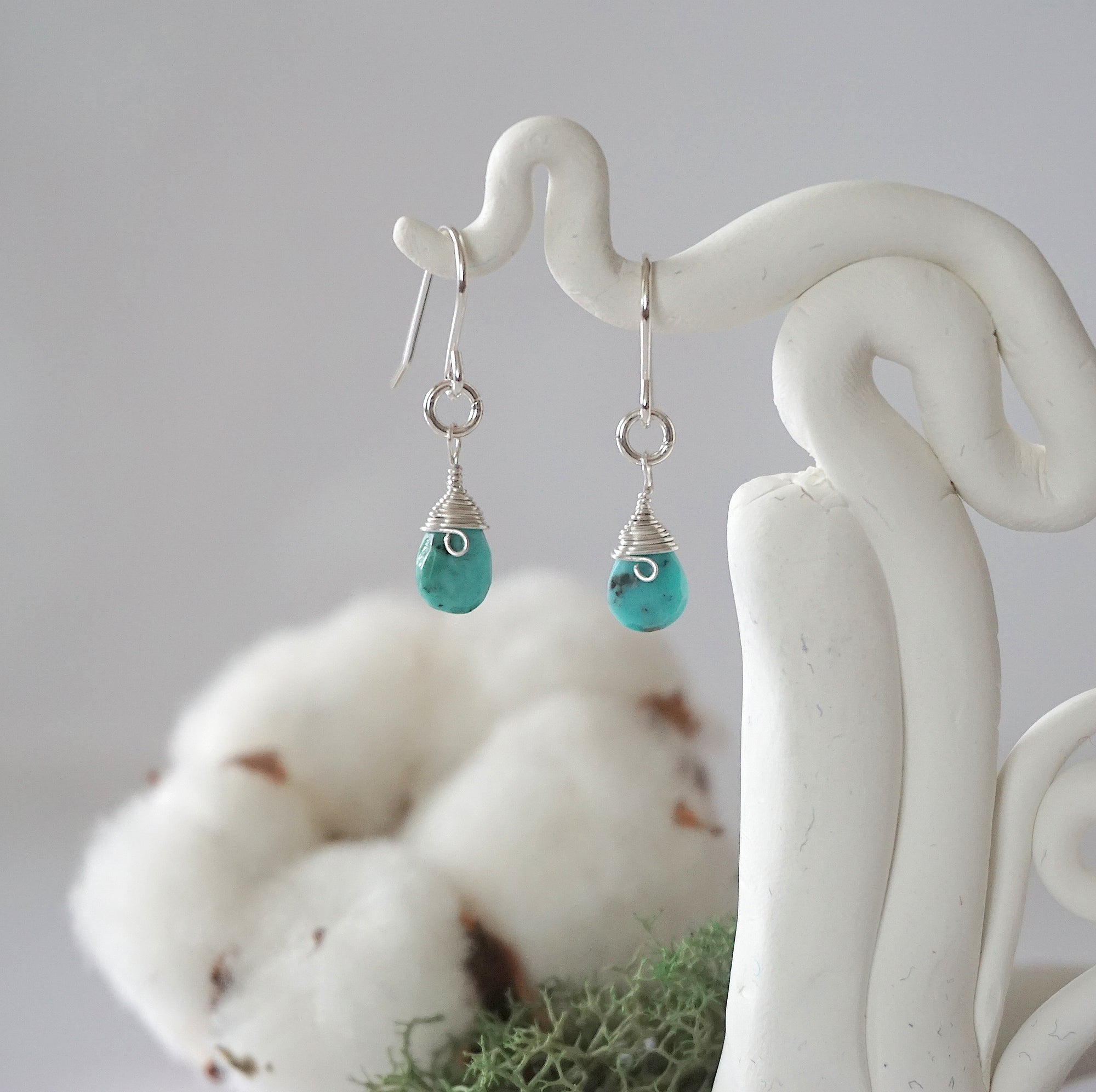 Detailed front view of handcrafted turquoise sterling silver drop earrings with natural faceted turquoise, artisan wire wrapping, hanging from a display – Designs by Nature Gems