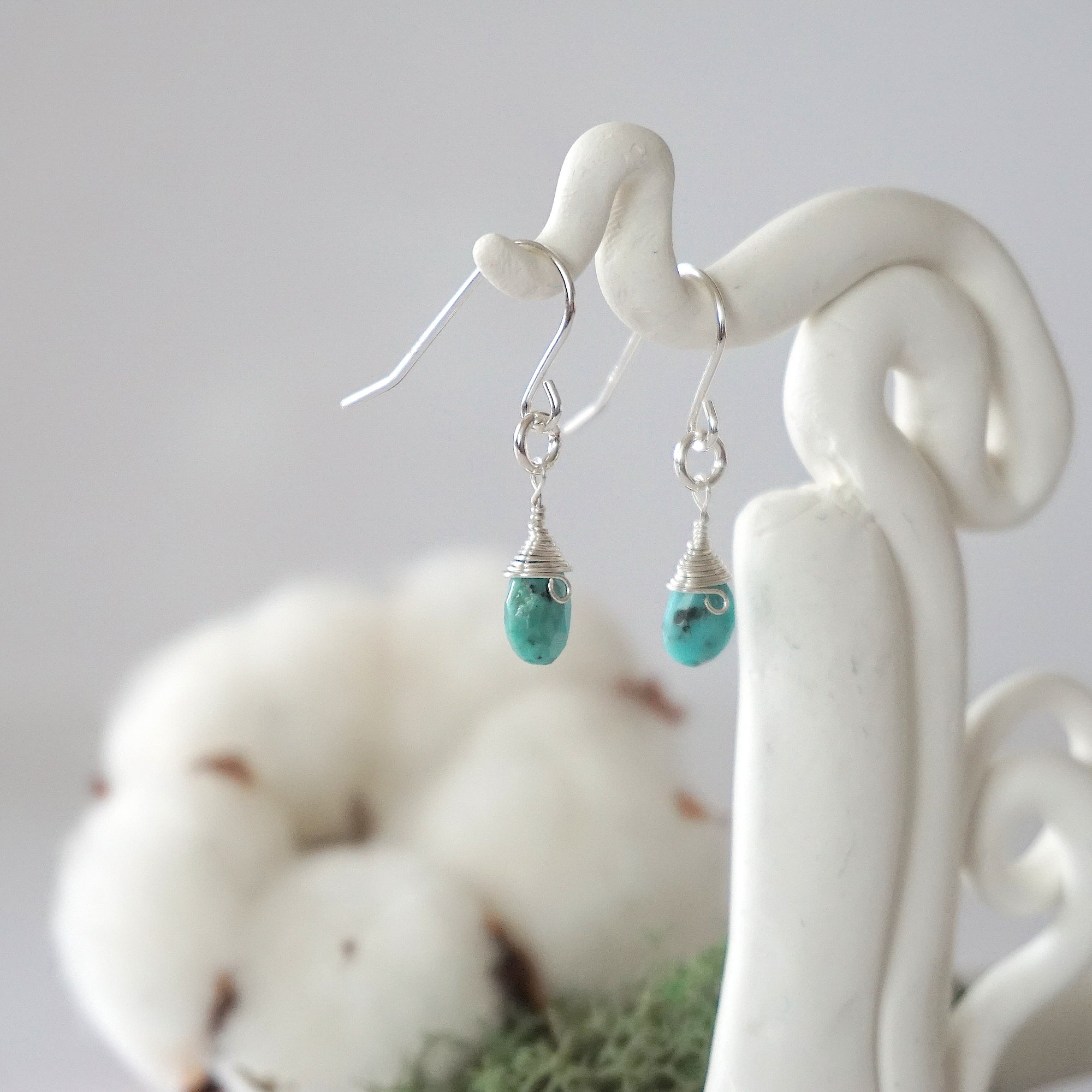 Side view of turquoise sterling silver drop earrings showing wire wrapped natural faceted turquoise, artisan craftsmanship, on a display – Designs by Nature Gems
