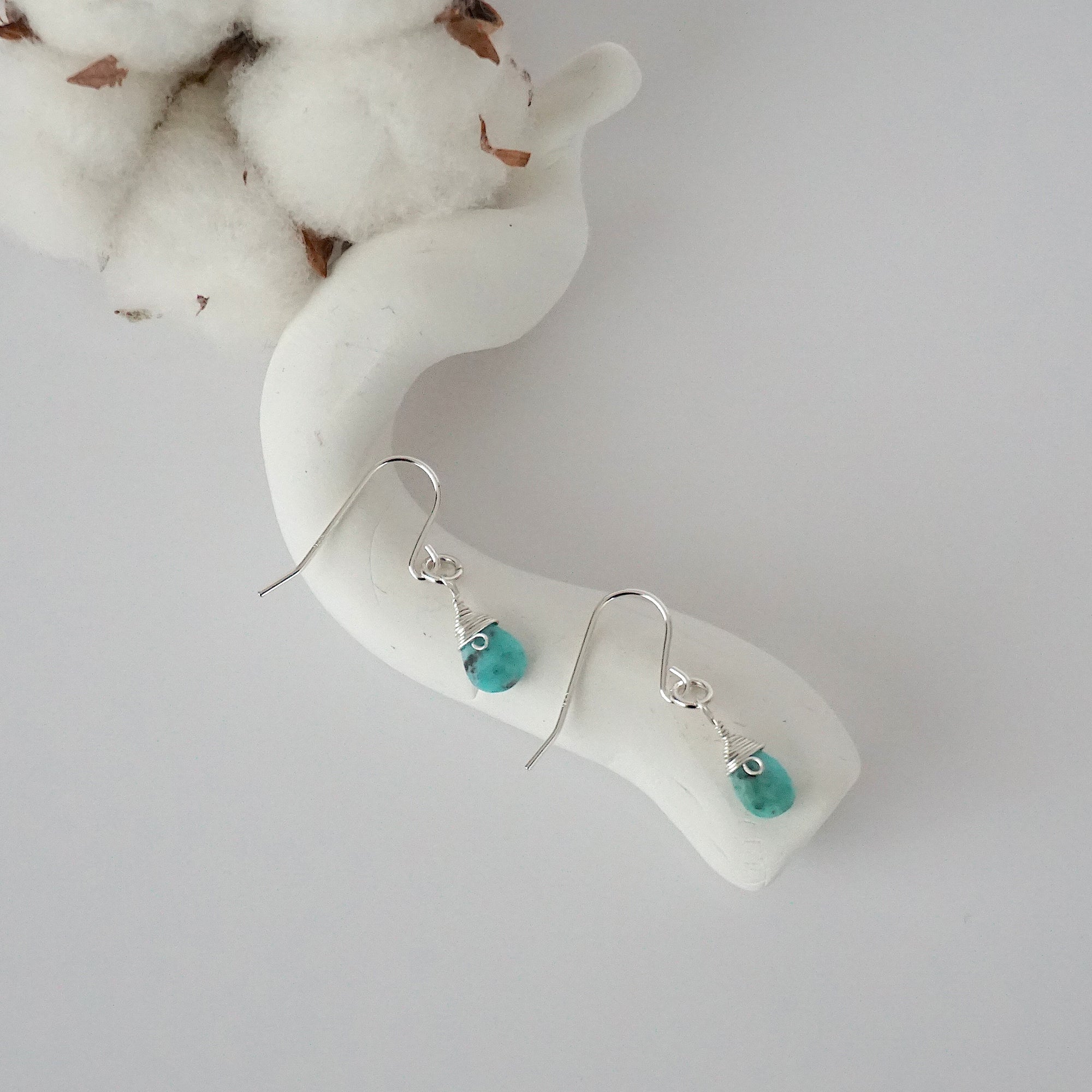 Turquoise sterling silver drop earrings with faceted natural turquoise stones and wire wrapping, laying flat on a display – Designs by Nature Gems