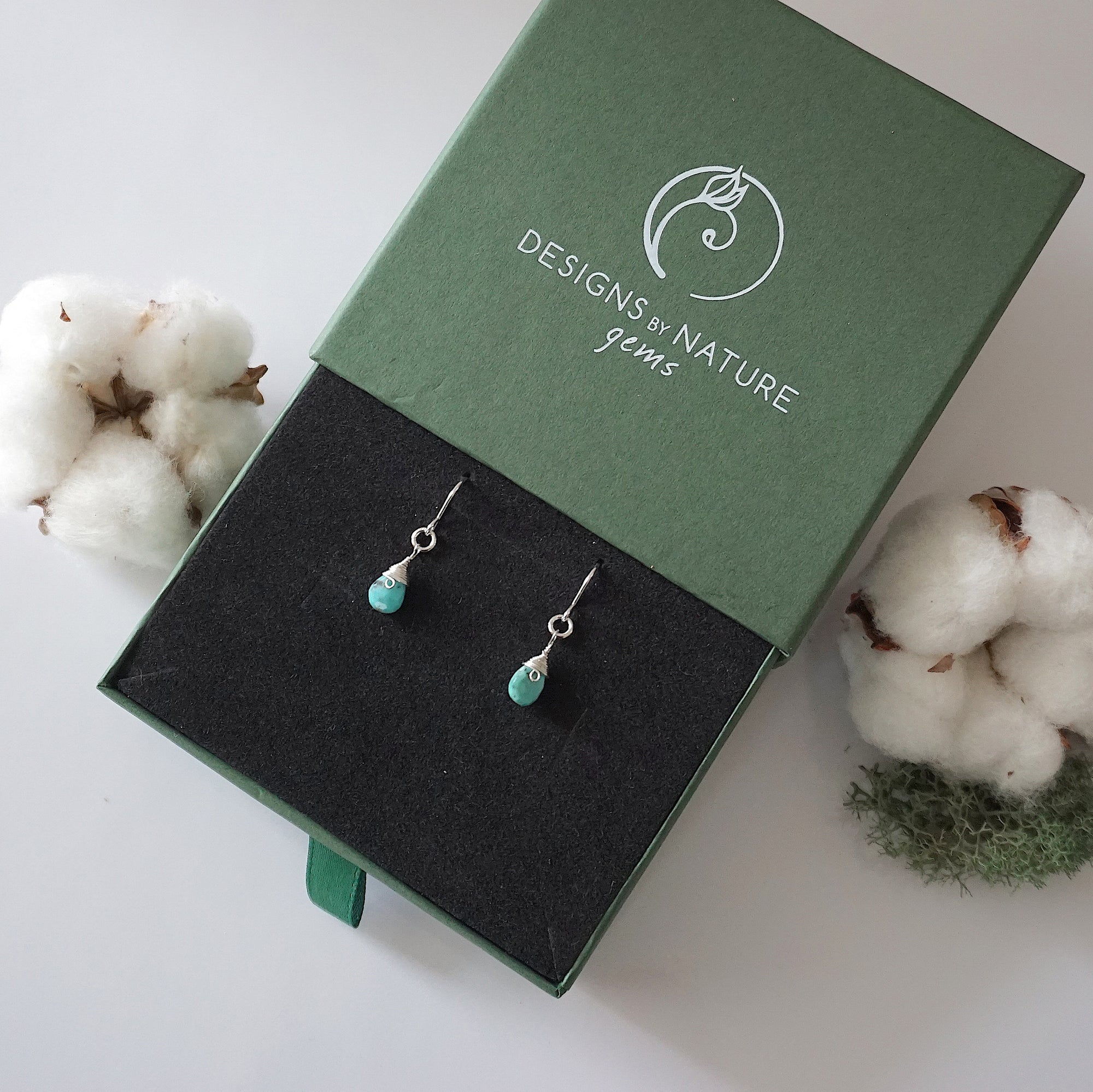 Turquoise sterling silver drop earrings in branded Designs by Nature Gems jewelry box, showcasing handcrafted faceted turquoise and sterling silver wire wrapping