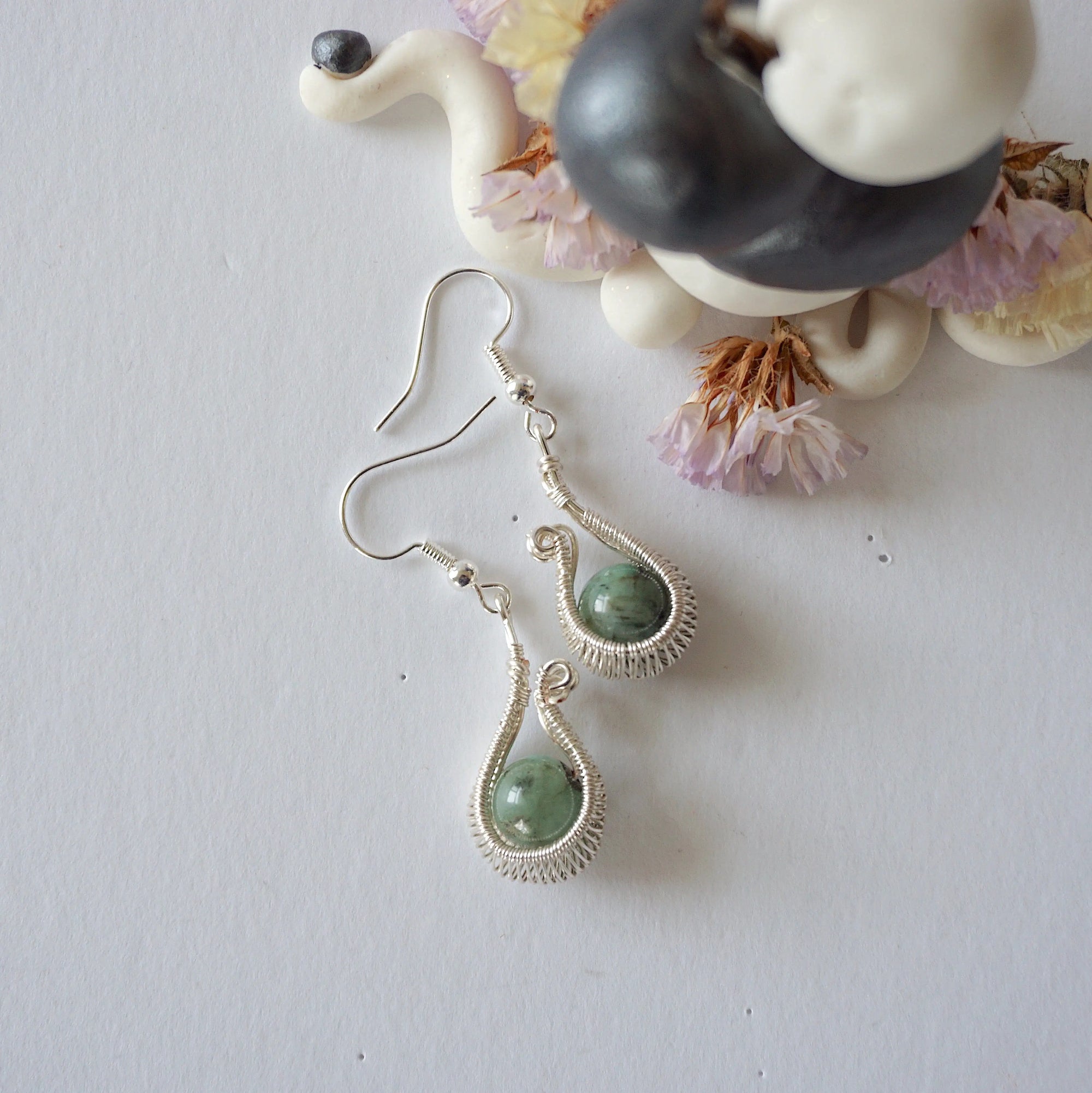 Emerald drop earrings on flat surface showing fish hook ear wire style and handcrafted wire wrapped emerald design