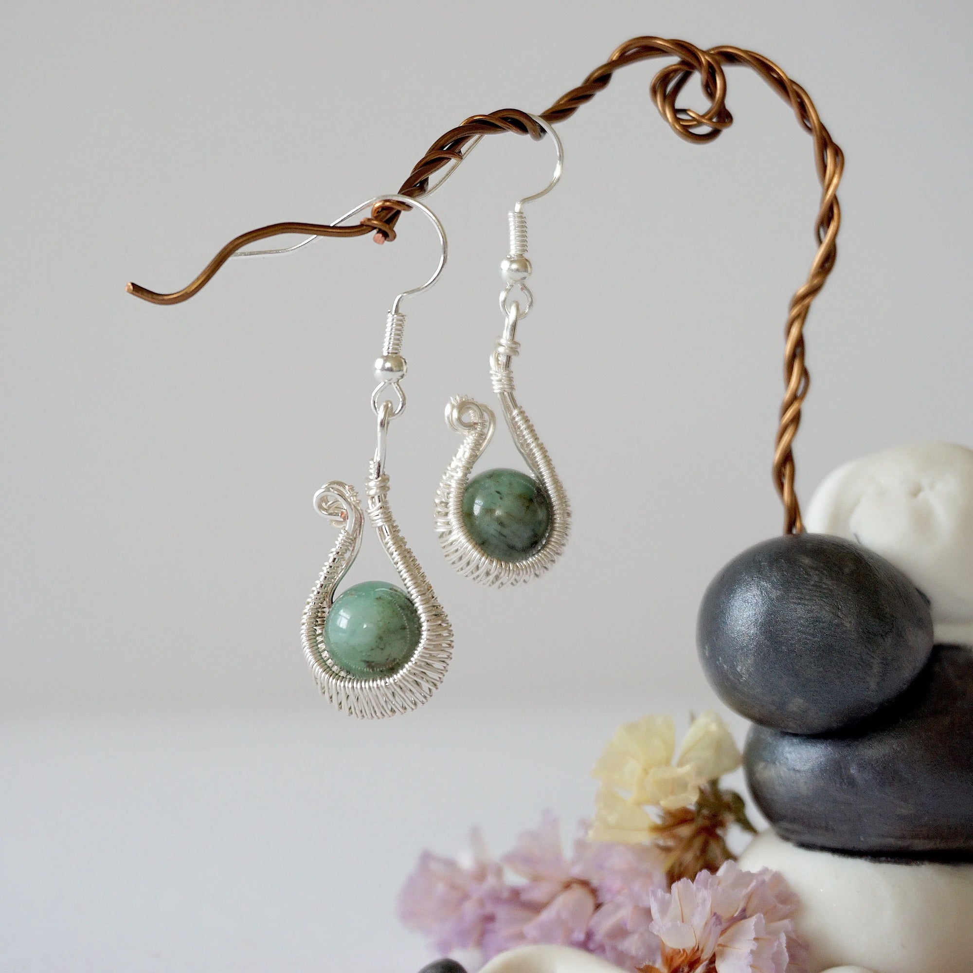 Close detail of wire wrapped emerald drop earrings showing intricate artisan wrapping around natural emerald bead