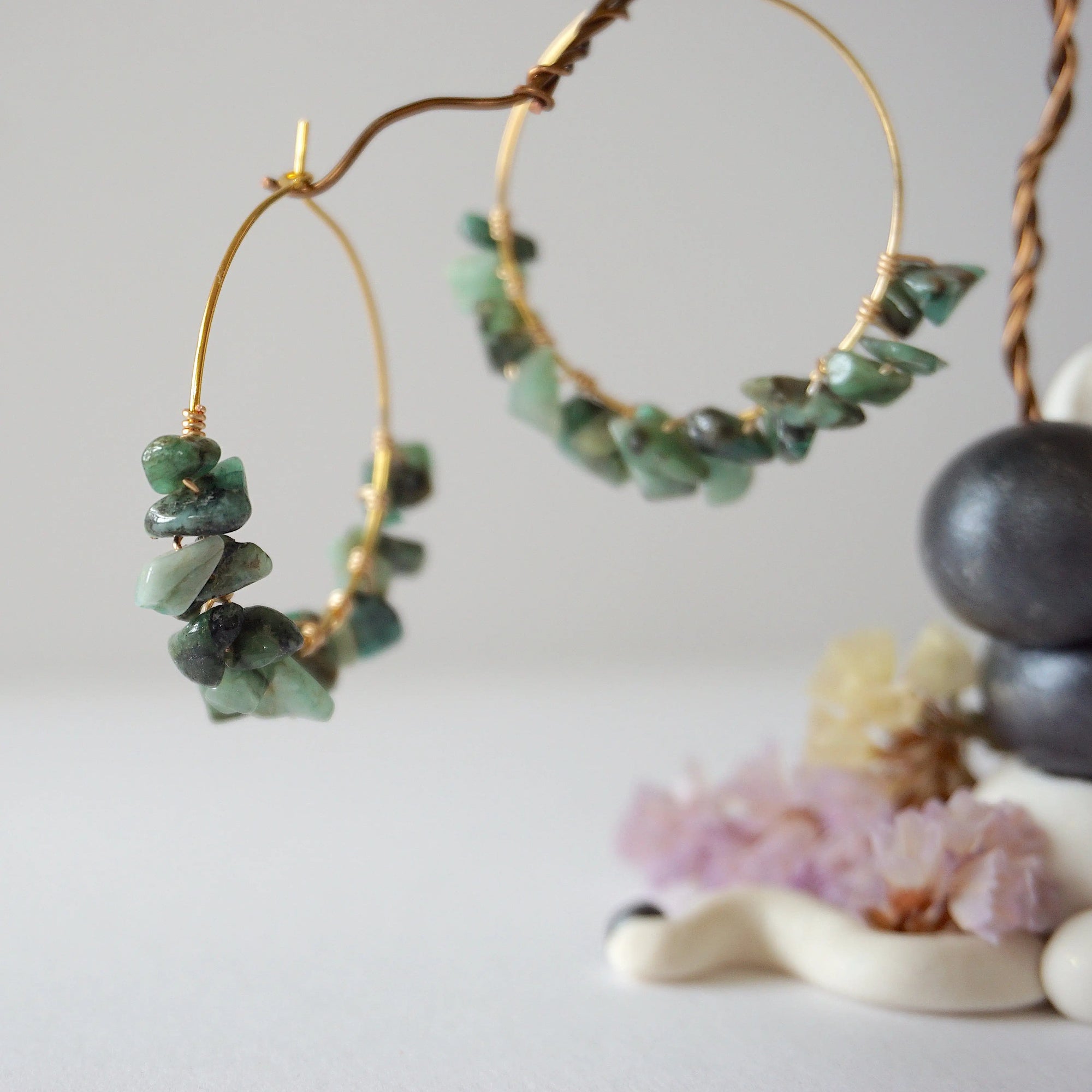Close detail of emerald hoop earrings showing natural emerald chips and artisan wire wrapping in warm gold copper