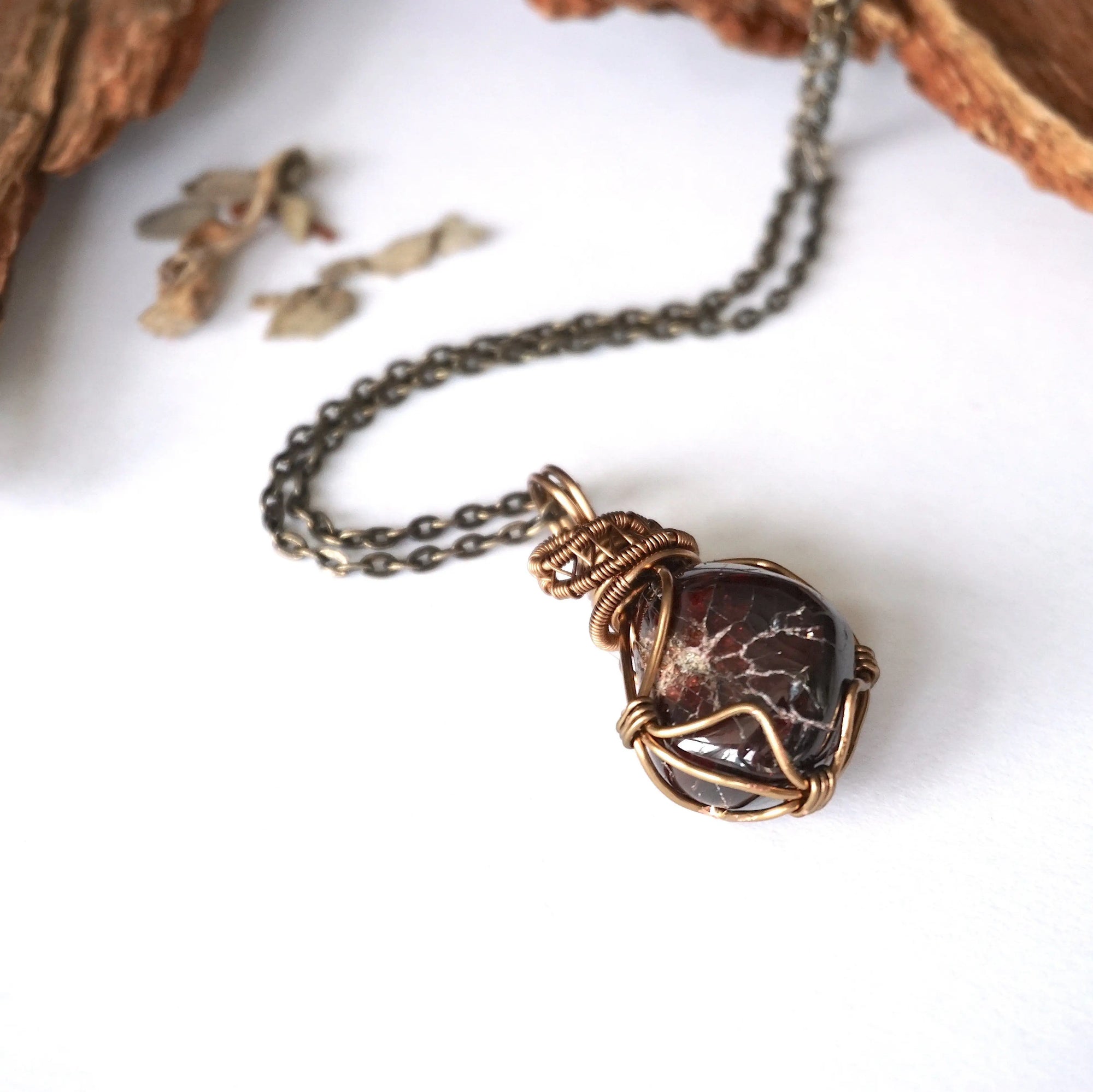 Women’s garnet wire wrapped necklace in antique bronze copper on an antique bronze chain, shown laying flat to highlight the natural garnet pendant
