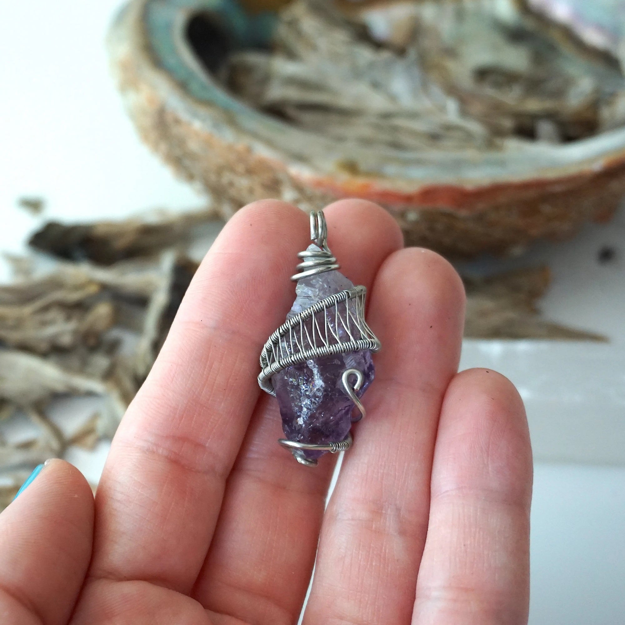Women’s raw amethyst pendant necklace shown in hand for size reference, white gold plated copper wire wrap