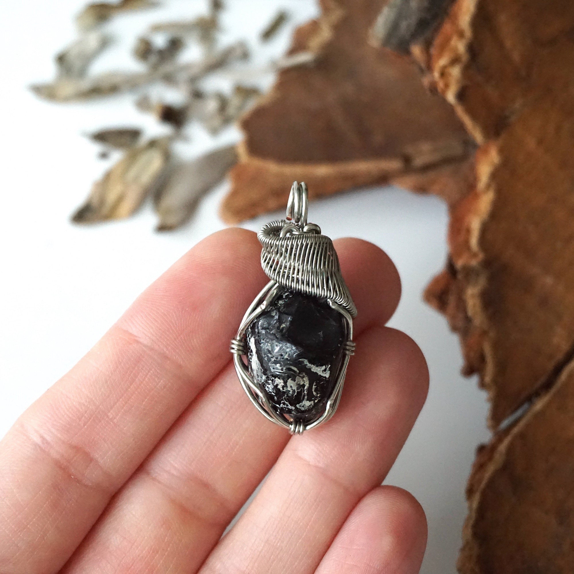 Apache tears obsidian pendant in hand for size reference – natural black volcanic glass, white gold copper wire, unisex jewelry by Designs by Nature Gems.