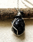 Angle view of apache tears obsidian necklace for men – highlighting unique artisan wire wrapping, glossy volcanic glass, white gold and black copper.