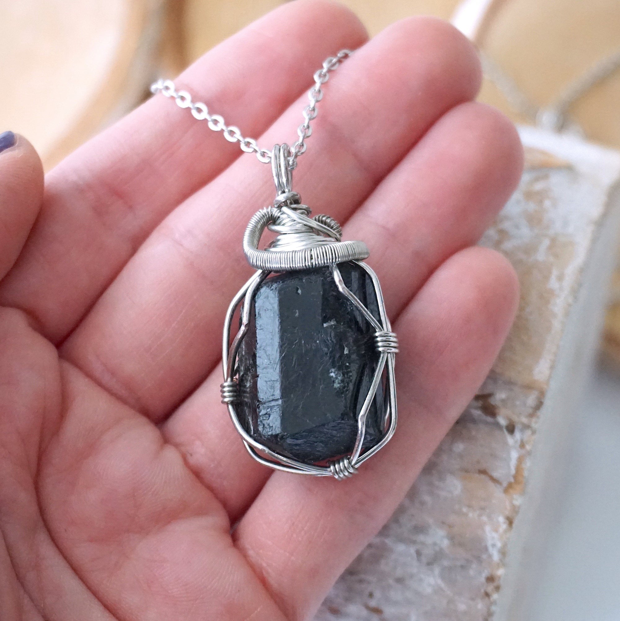Raw black tourmaline necklace for men in hand – size reference, showcases natural black stone and artisan wire wrapping.