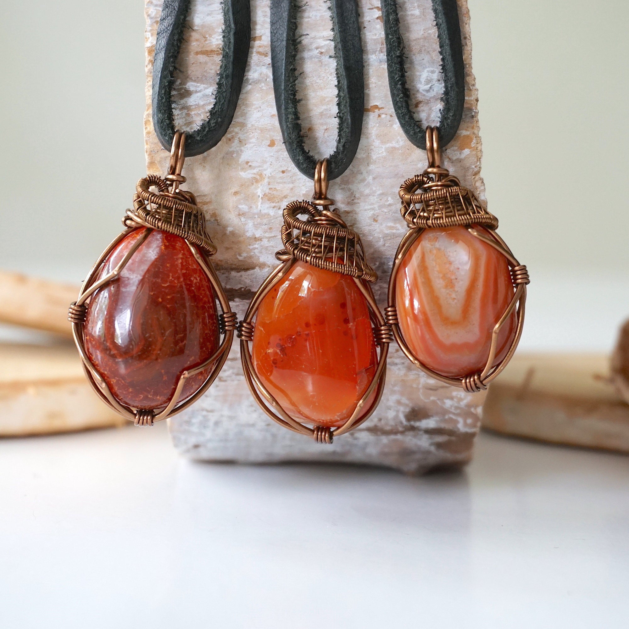 hree raw carnelian pendants for men – showing natural variation in size, shape, and orange shade, black leather cord.