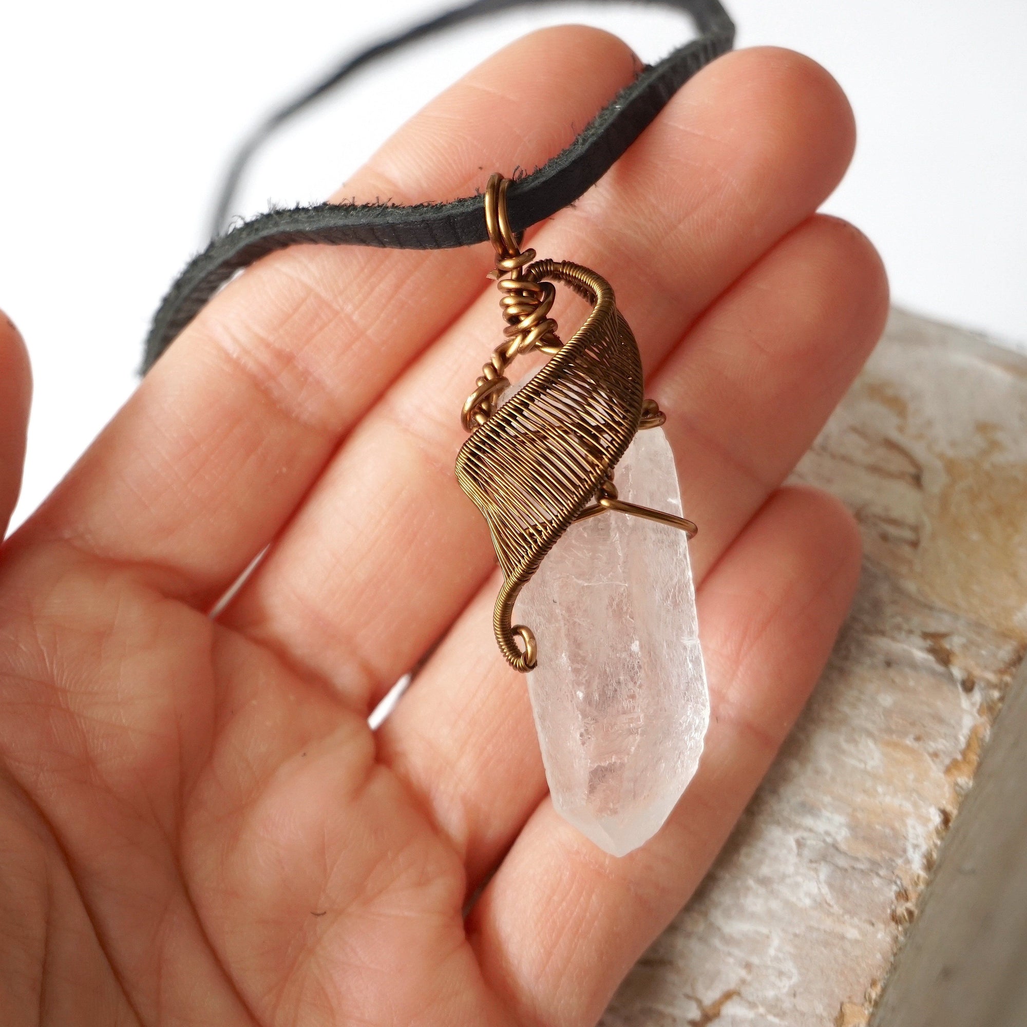 Clear quartz point pendant in hand for size reference – natural crystal, antique bronze copper wire, April birthstone, masculine design.