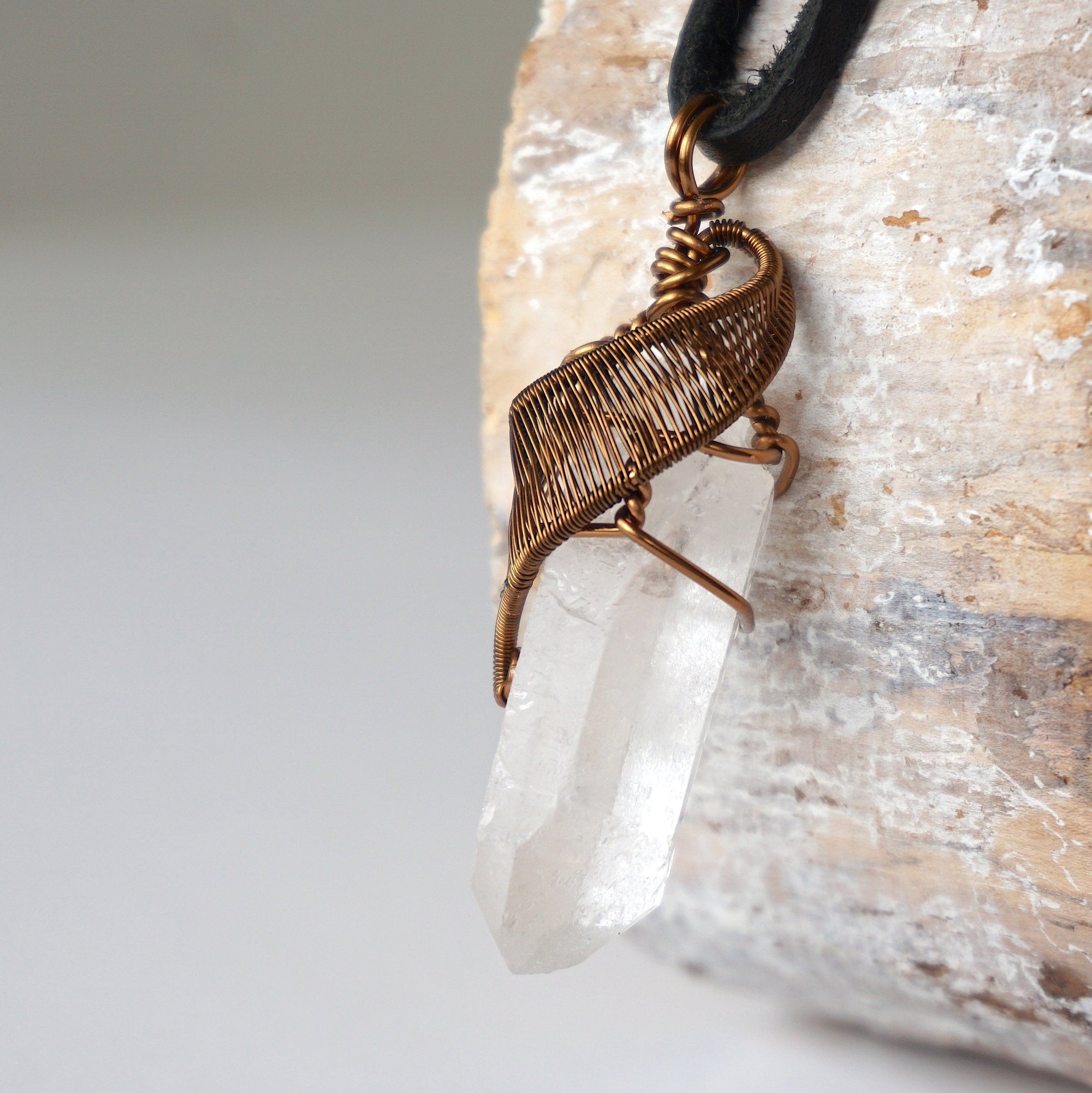Left angle close-up of clear quartz point necklace for men – highlighting unique wire-wrapped artistry, clear quartz, black leather cord.