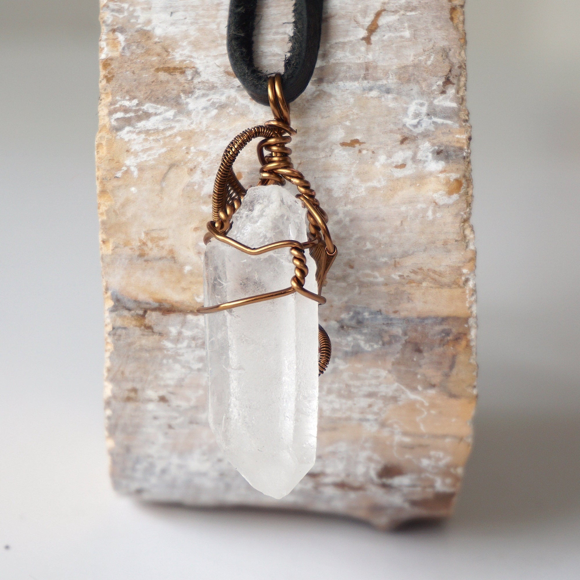 Back view of handcrafted clear quartz point necklace for men – natural stone and wire wrapping, April birthstone, black leather cord.