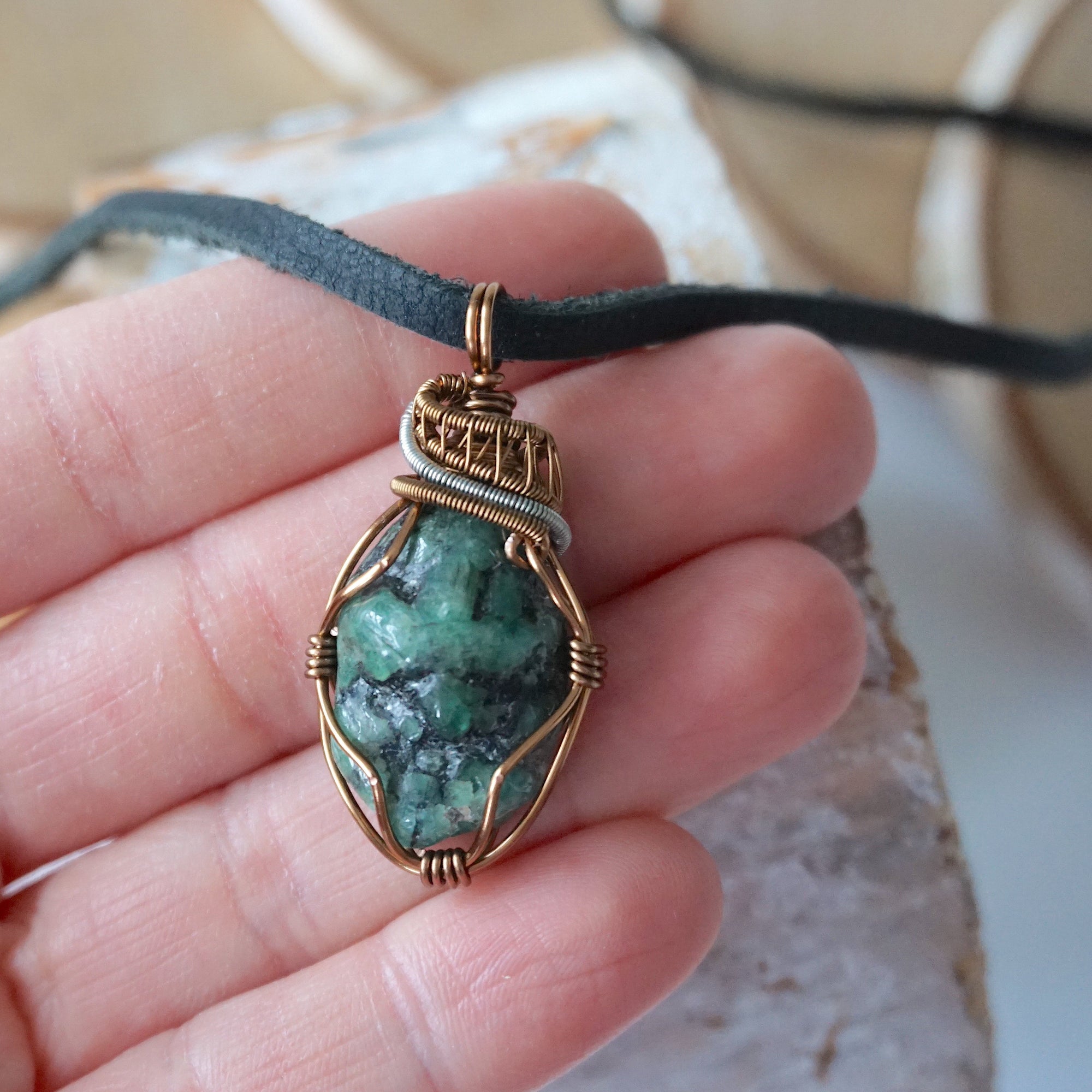 Raw emerald pendant for men shown in hand for size reference – natural green crystal, artisan wire, black leather cord.