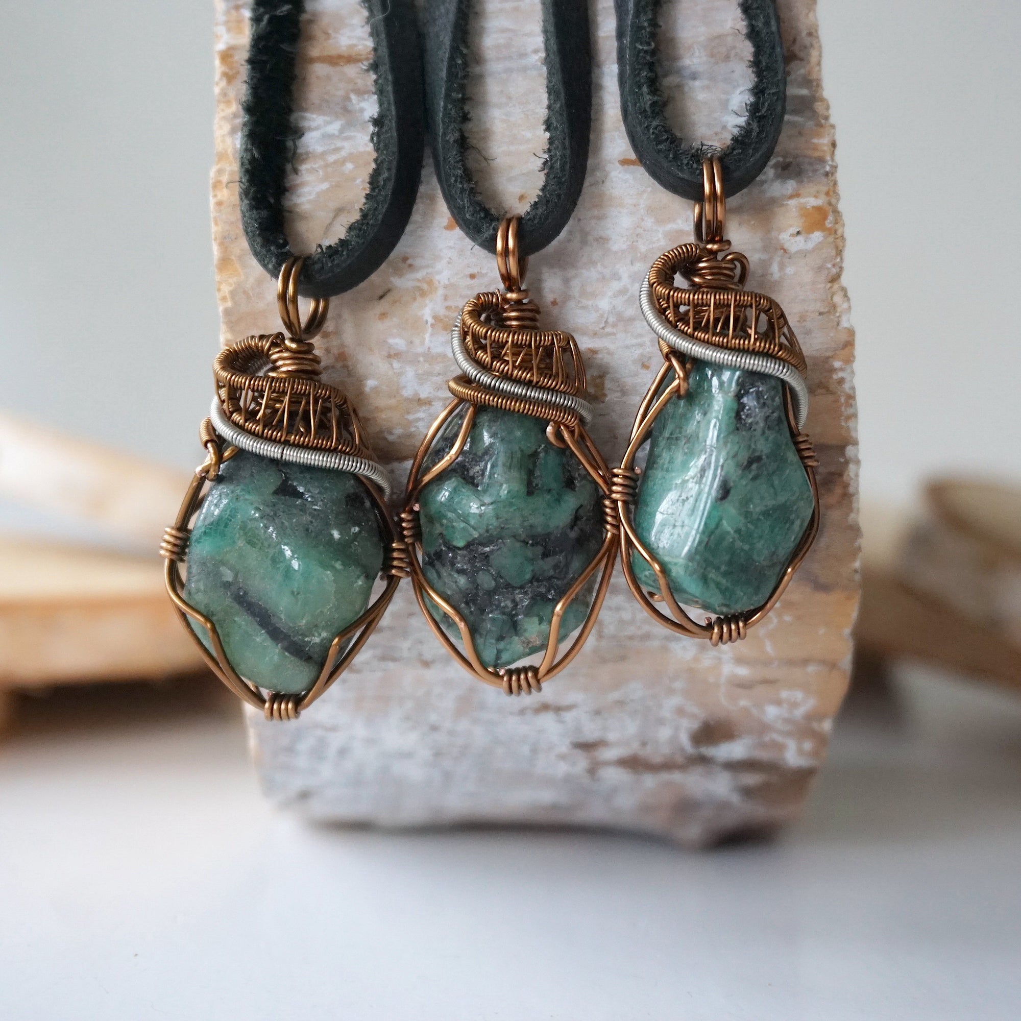Three raw emerald pendants for men – showing natural variation in size, shape, and green shade, black leather cord.