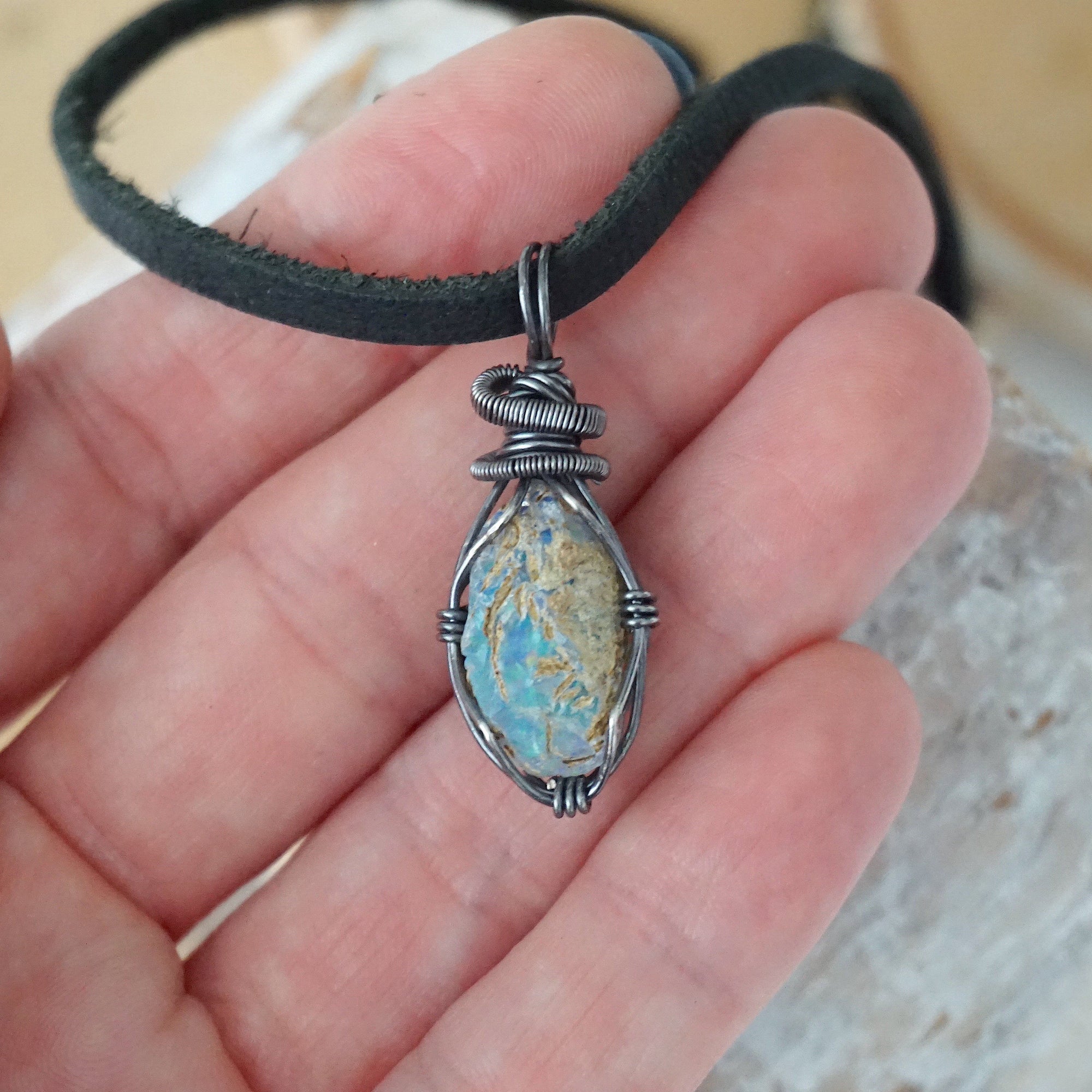 Raw opal pendant for men shown in hand for size reference – natural Ethiopian fire opal, antiqued sterling silver wire, black leather cord.