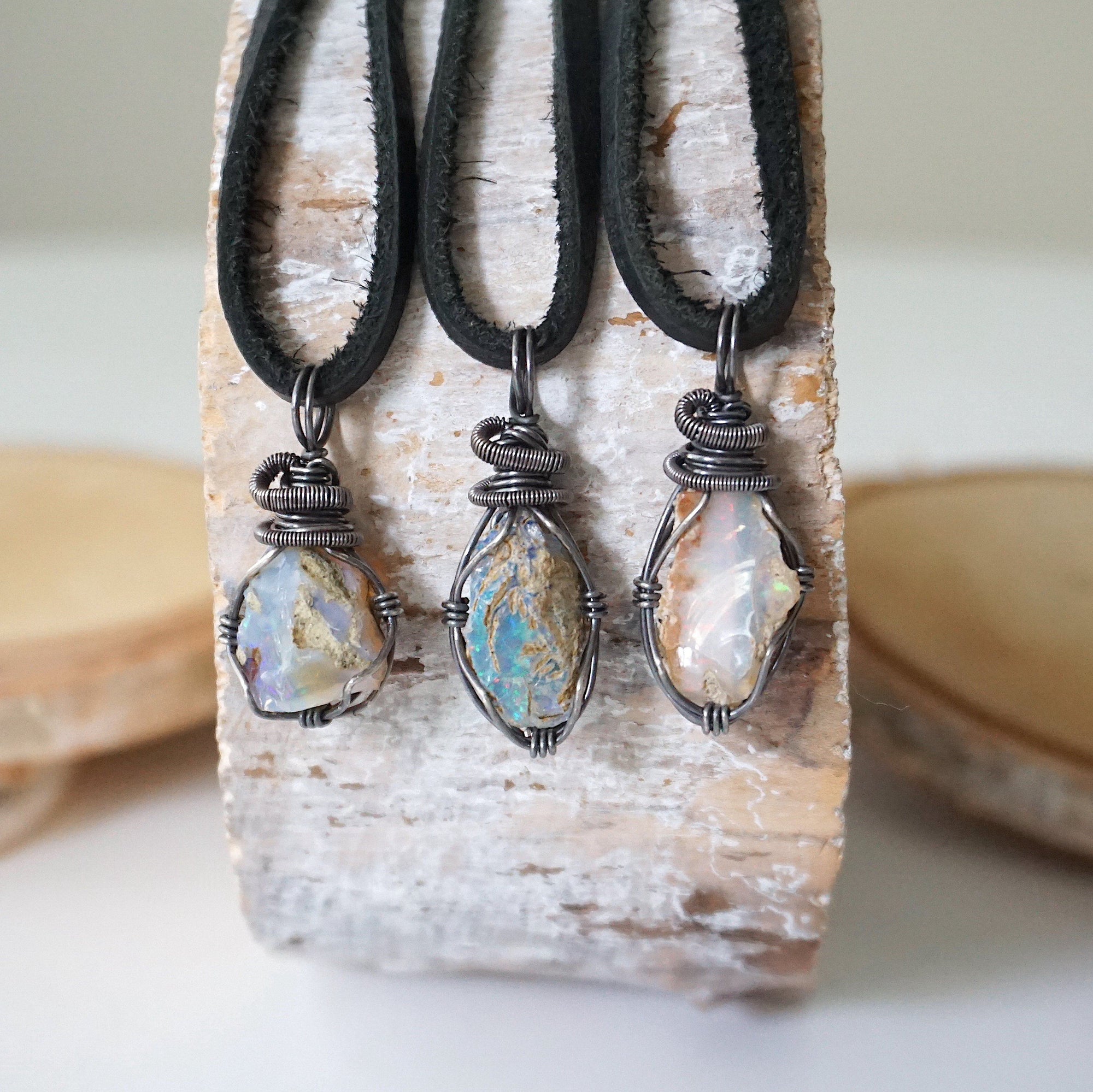 Three raw opal pendants for men – showing natural variation in size, shape, and color, handcrafted with antiqued sterling silver wire.