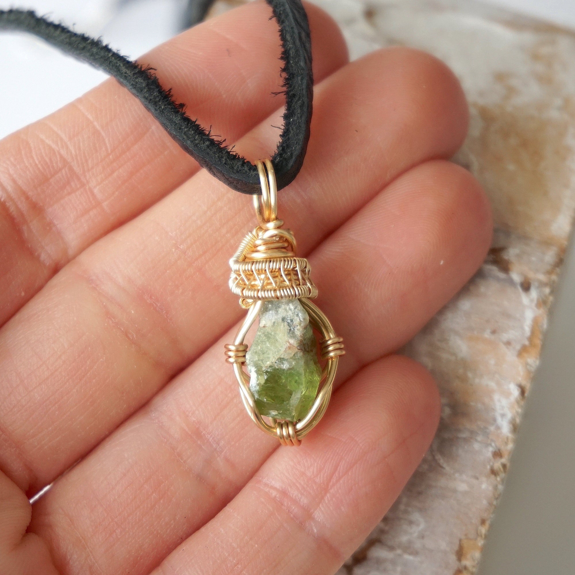 Raw peridot necklace for men in hand – size reference, showcases natural green stone and artisan wire wrapping.
