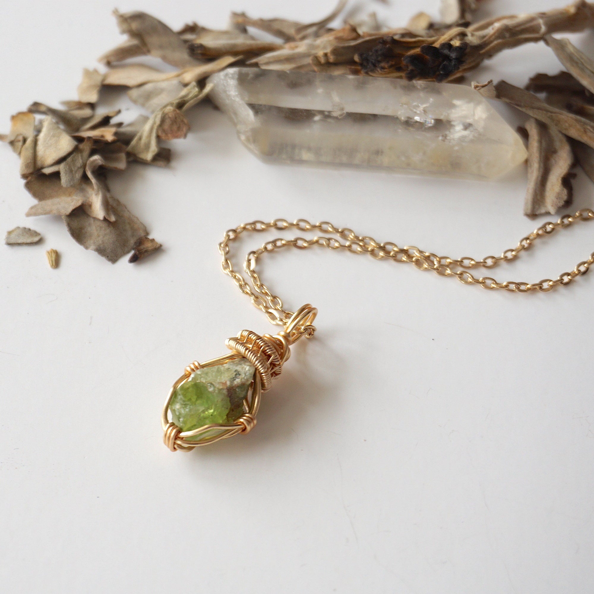 Raw peridot necklace for women on gold plated brass chain, flat lay – artisan gold copper wire wrapping, natural August birthstone pendant.
