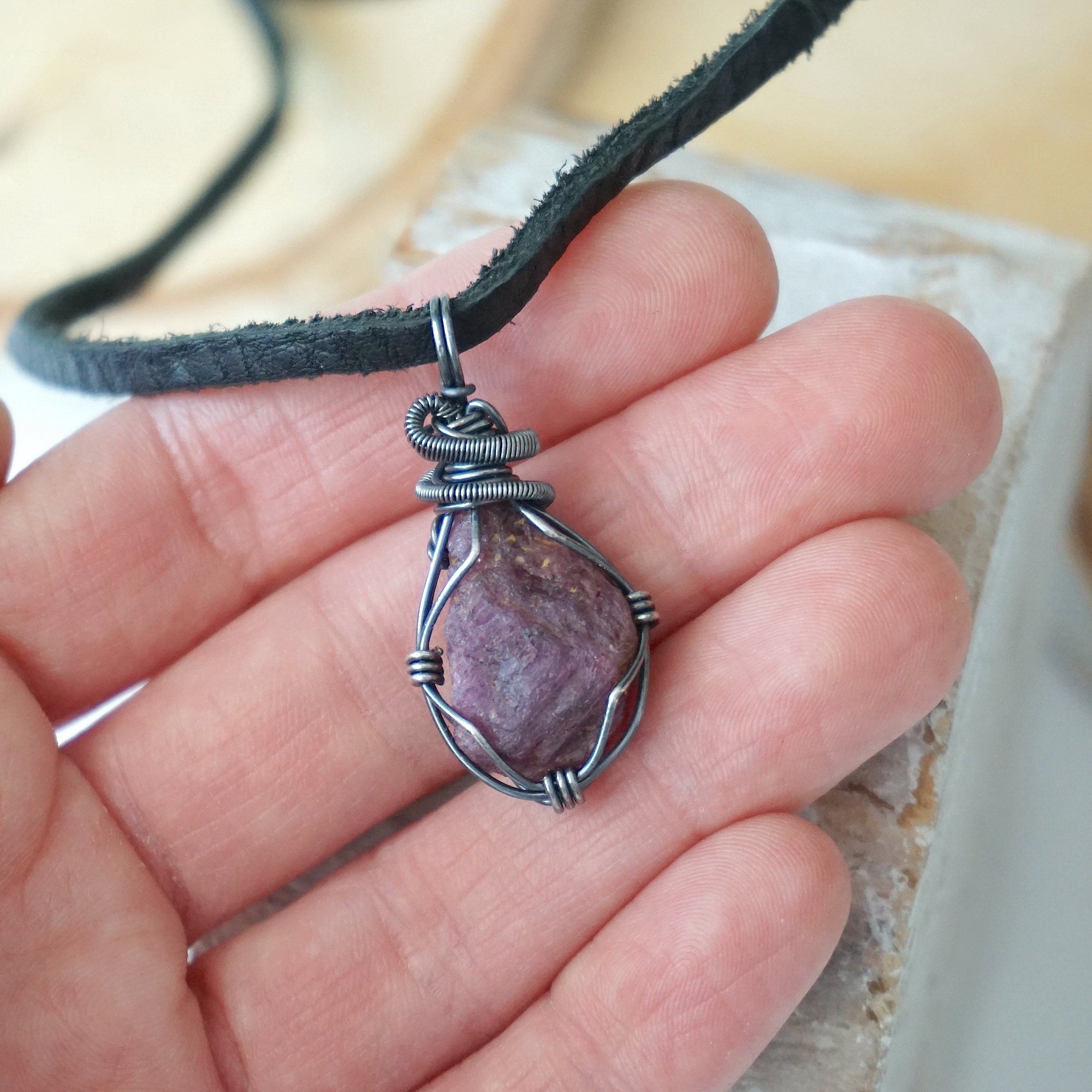 Ruby pendant for men in hand for size reference – natural red crystal, antiqued sterling silver wire, black leather cord, July birthstone.