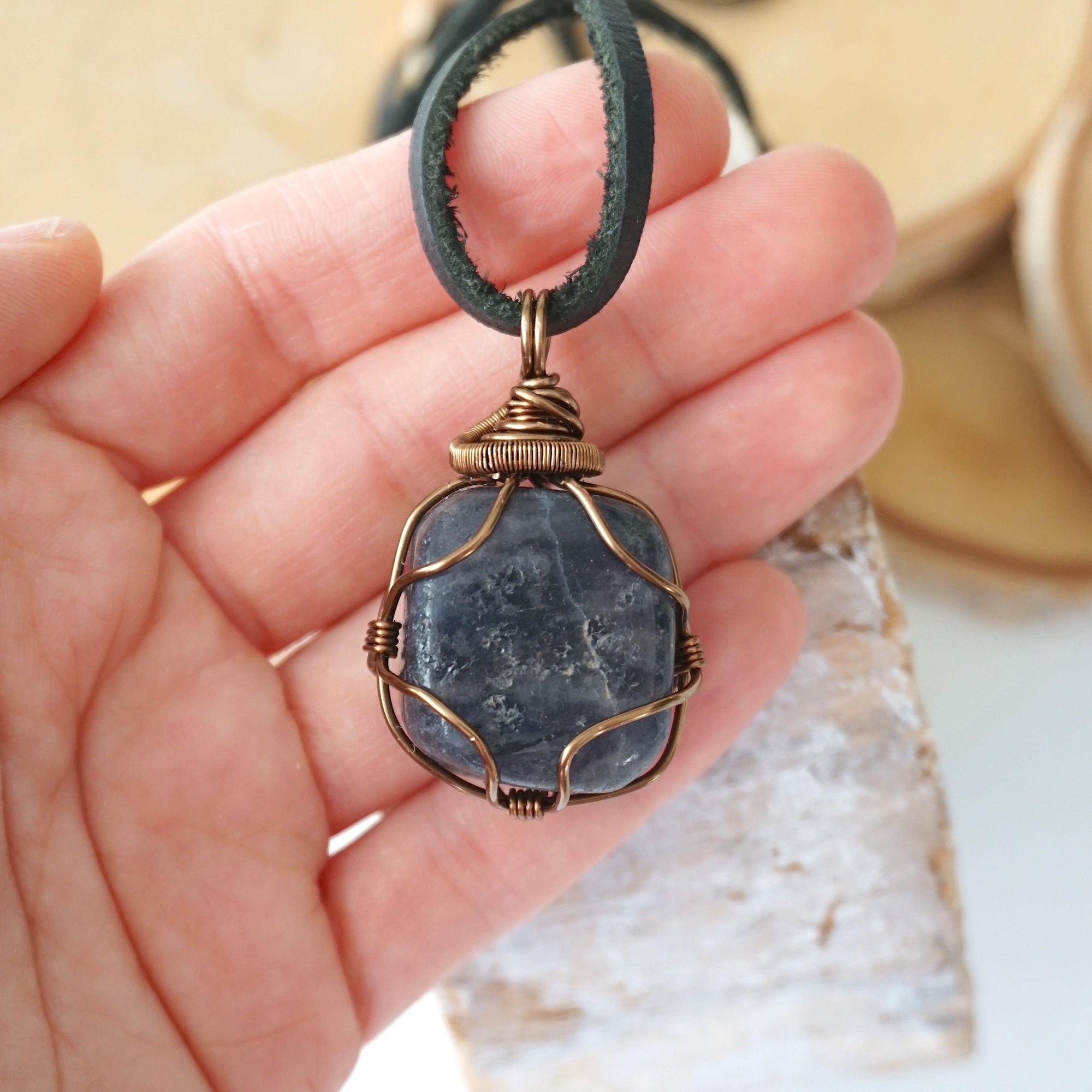 Sapphire pendant for men in hand for size reference – genuine raw sapphire, bronze copper wire, black leather cord, September birthstone.