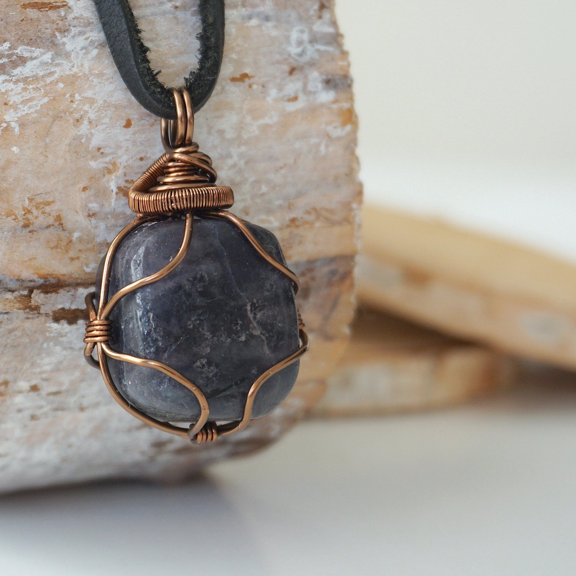Right angle close-up of men's sapphire necklace – detailed bronze copper wire wrapping, raw blue sapphire, black leather cord.