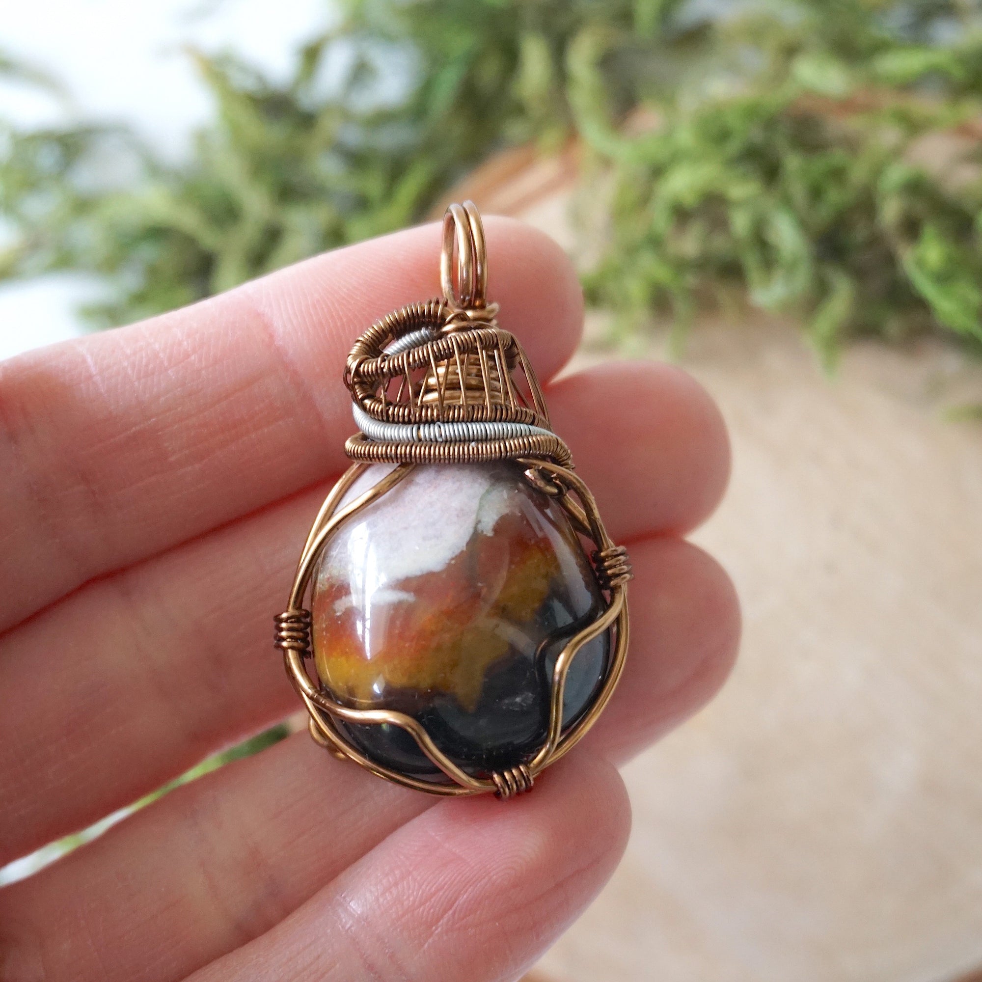Sardonyx pendant in hand for size reference – natural banded stone, bronze and dark silver copper wire, unisex birthstone jewelry by Designs by Nature Gems.