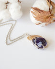 Detailed front view of women’s amethyst necklace, polished dark amethyst pendant, artisan wire wrapped in silver and gold plated copper