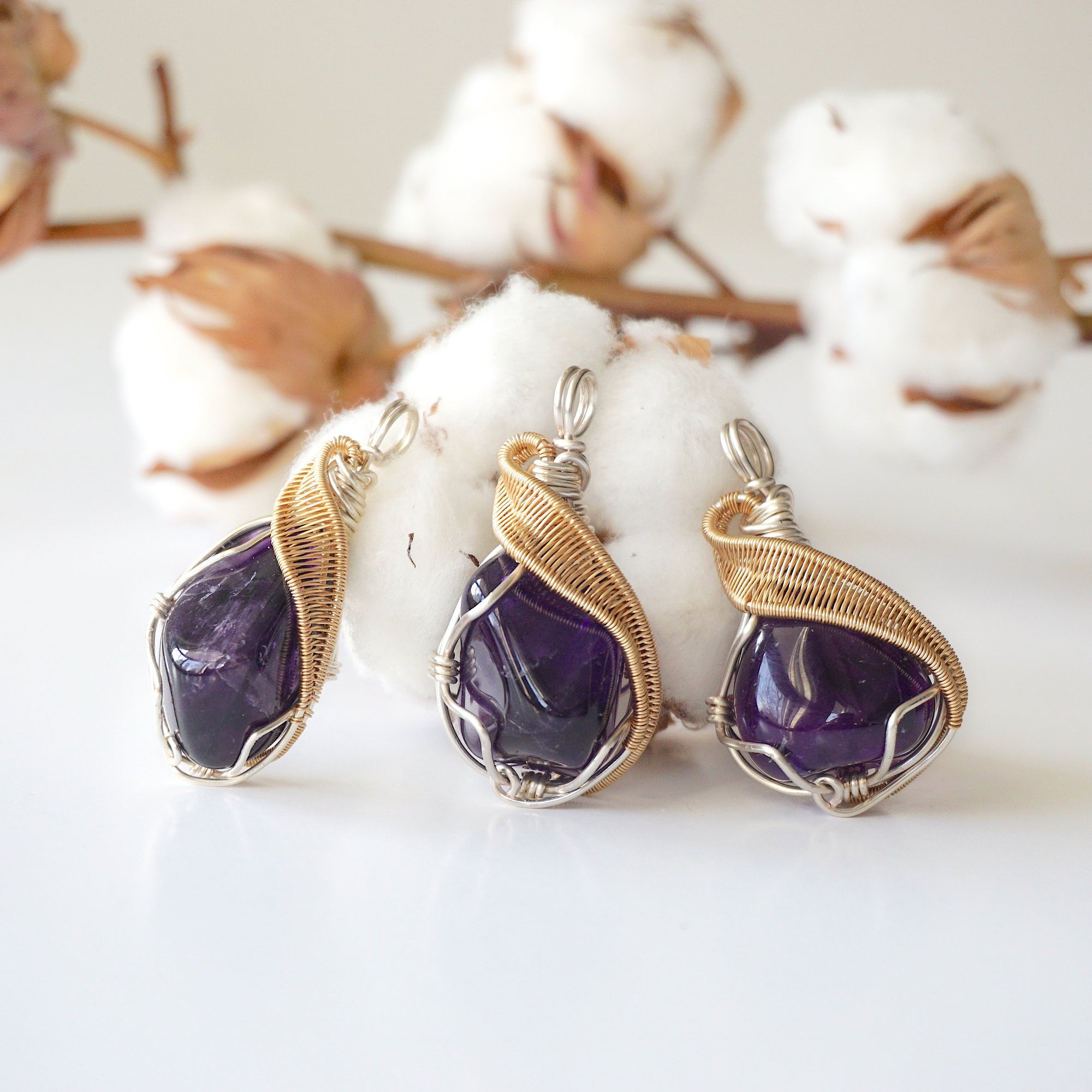 Three women’s amethyst pendants showing natural variation in stone size, shape, and color, silver and gold plated copper artisan wire wrap