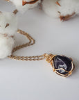 Detailed front view of women’s polished dark amethyst pendant on gold chain, artisan wire wrapped in gold plated copper