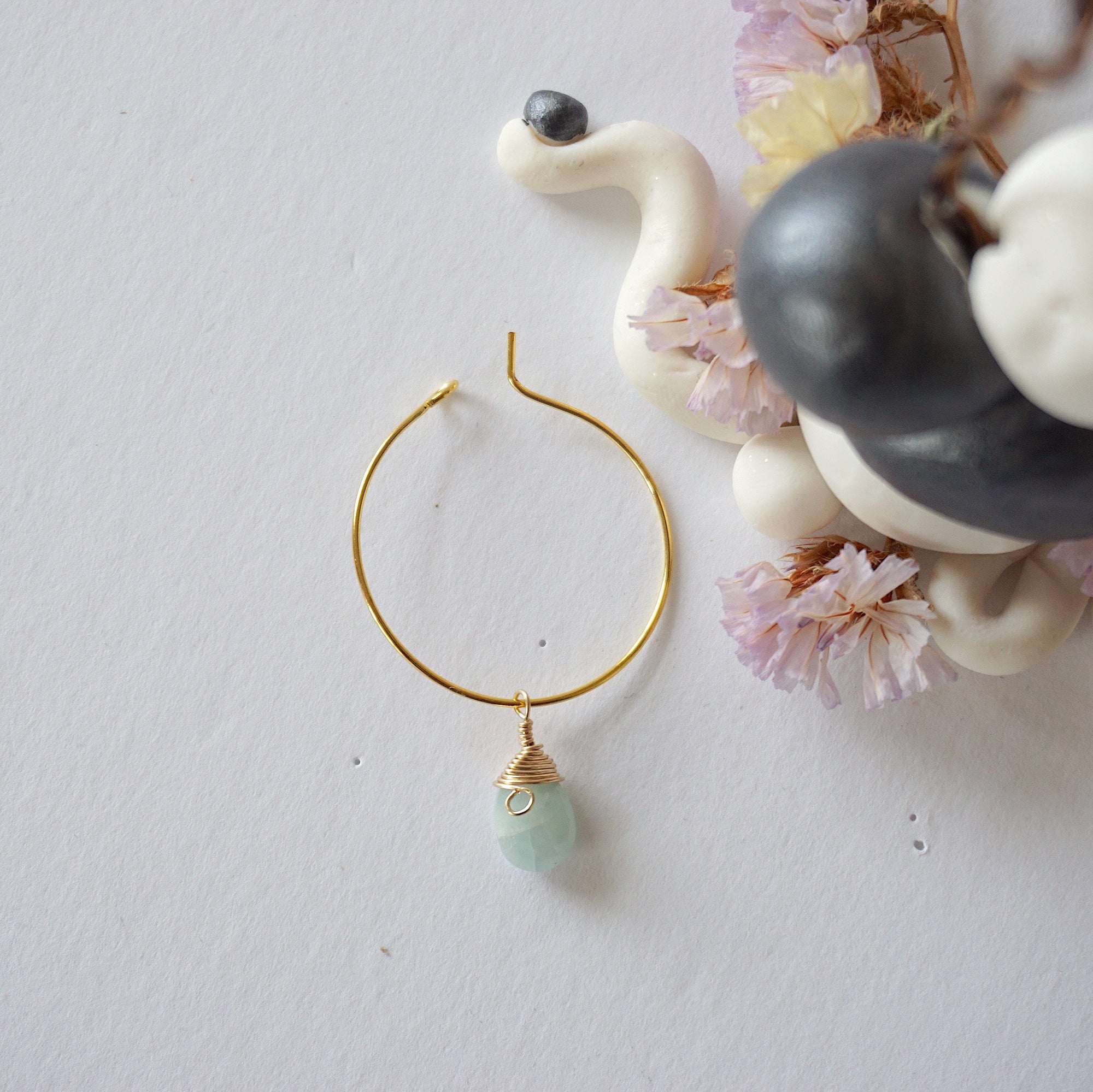Flat lay of a gold plated aquamarine hoop drop earring, highlighting the wire wrapped natural aquamarine gemstone and minimalist hoop design