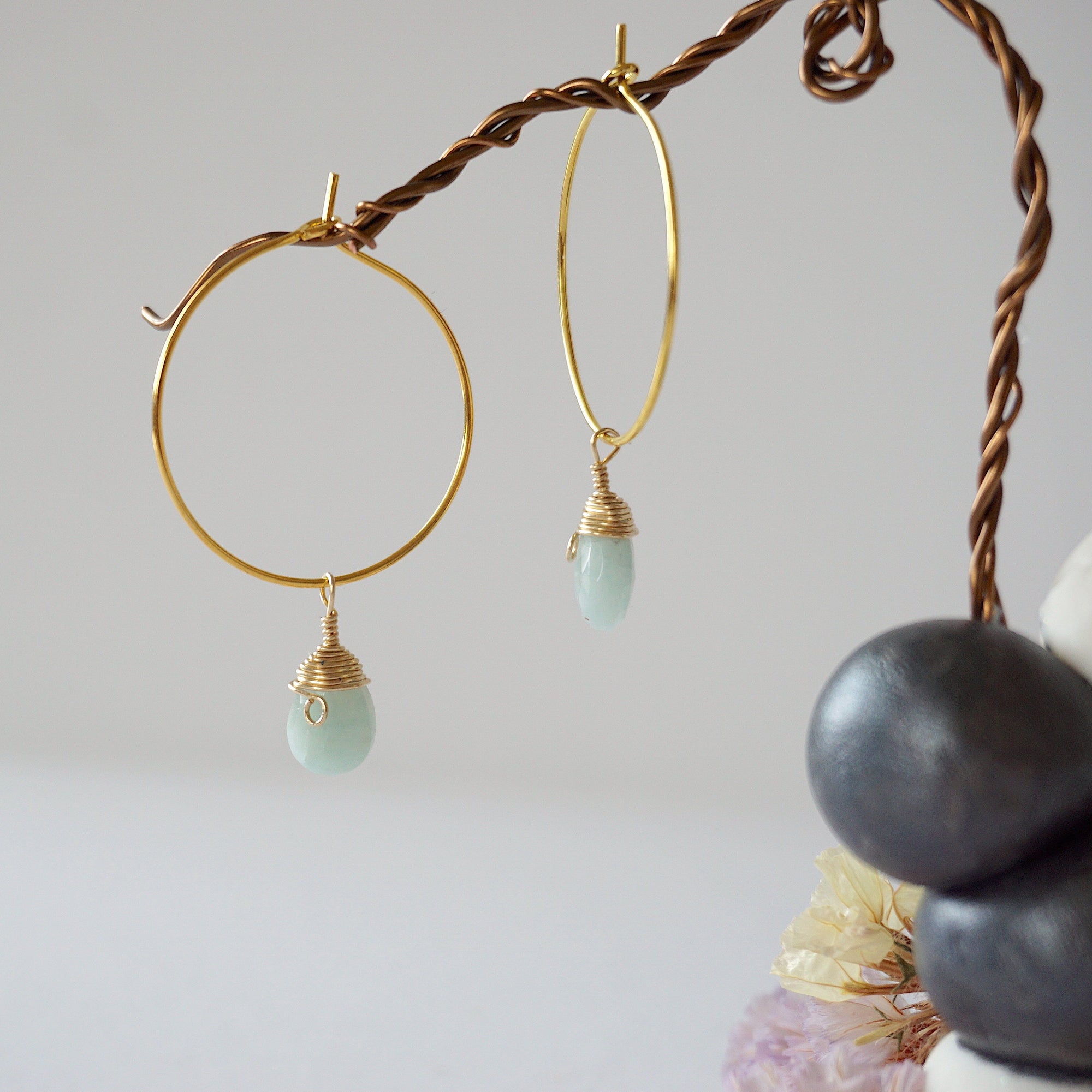Close-up of handcrafted aquamarine hoop drop earrings in gold plated brass, featuring wire wrapped natural blue aquamarine gemstones on a jewelry display