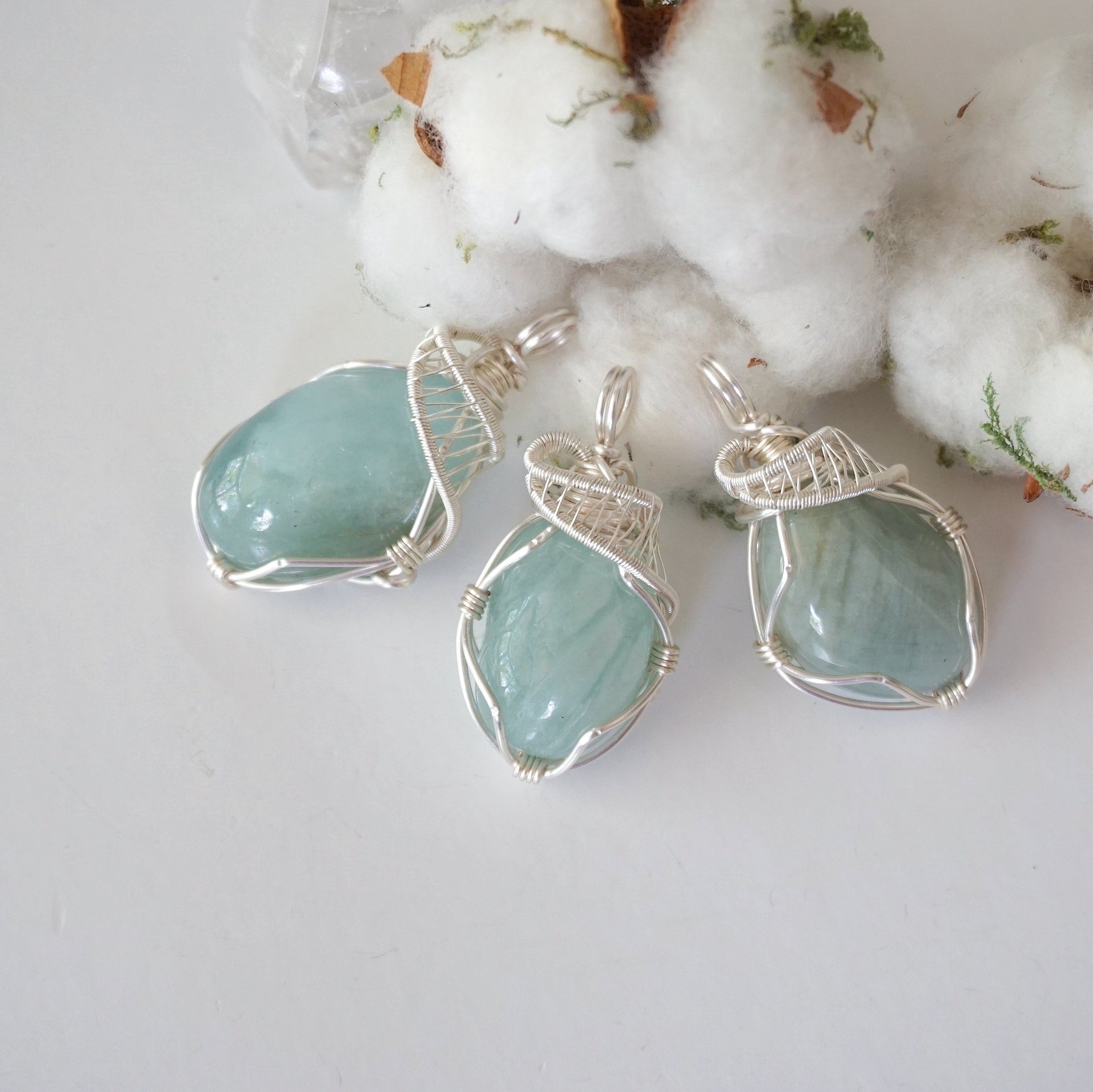 Three aquamarine pendants showing natural variation in size, shape, and blue color, artisan wire wrapped, soft silver over copper