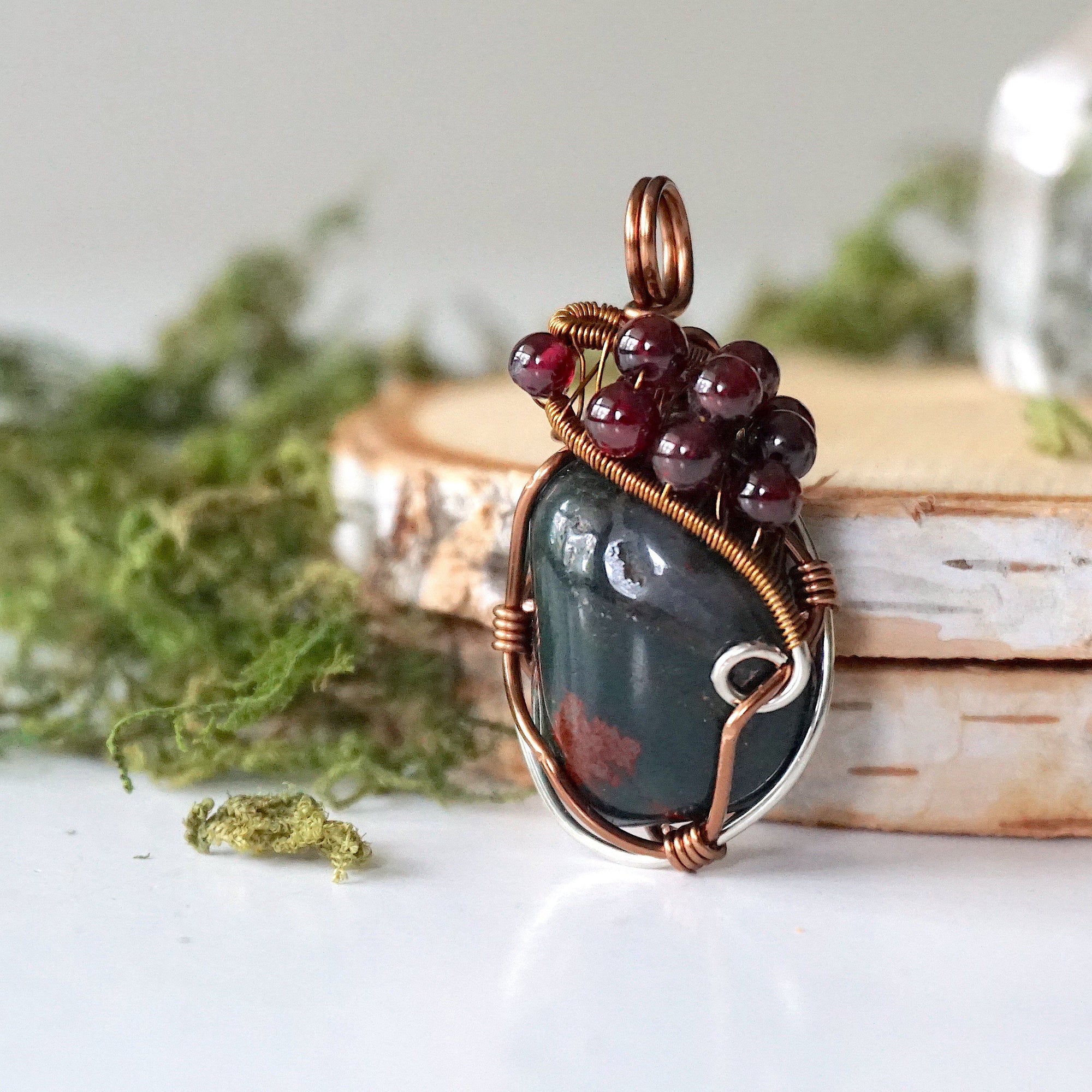 Detailed side view of a bloodstone pendant showing antique bronze and tin plated copper wire wrapping with garnet accents