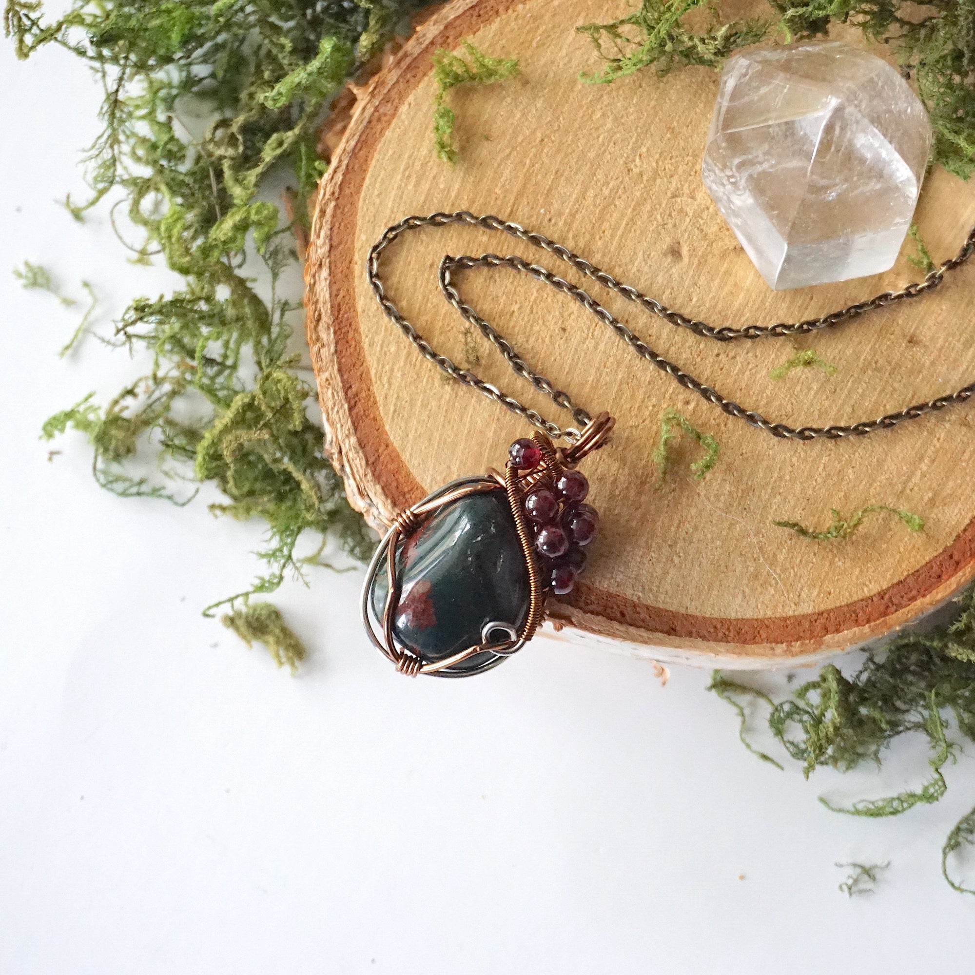 Bloodstone pendant necklace with garnet accents on an antique bronze chain, shown laying flat