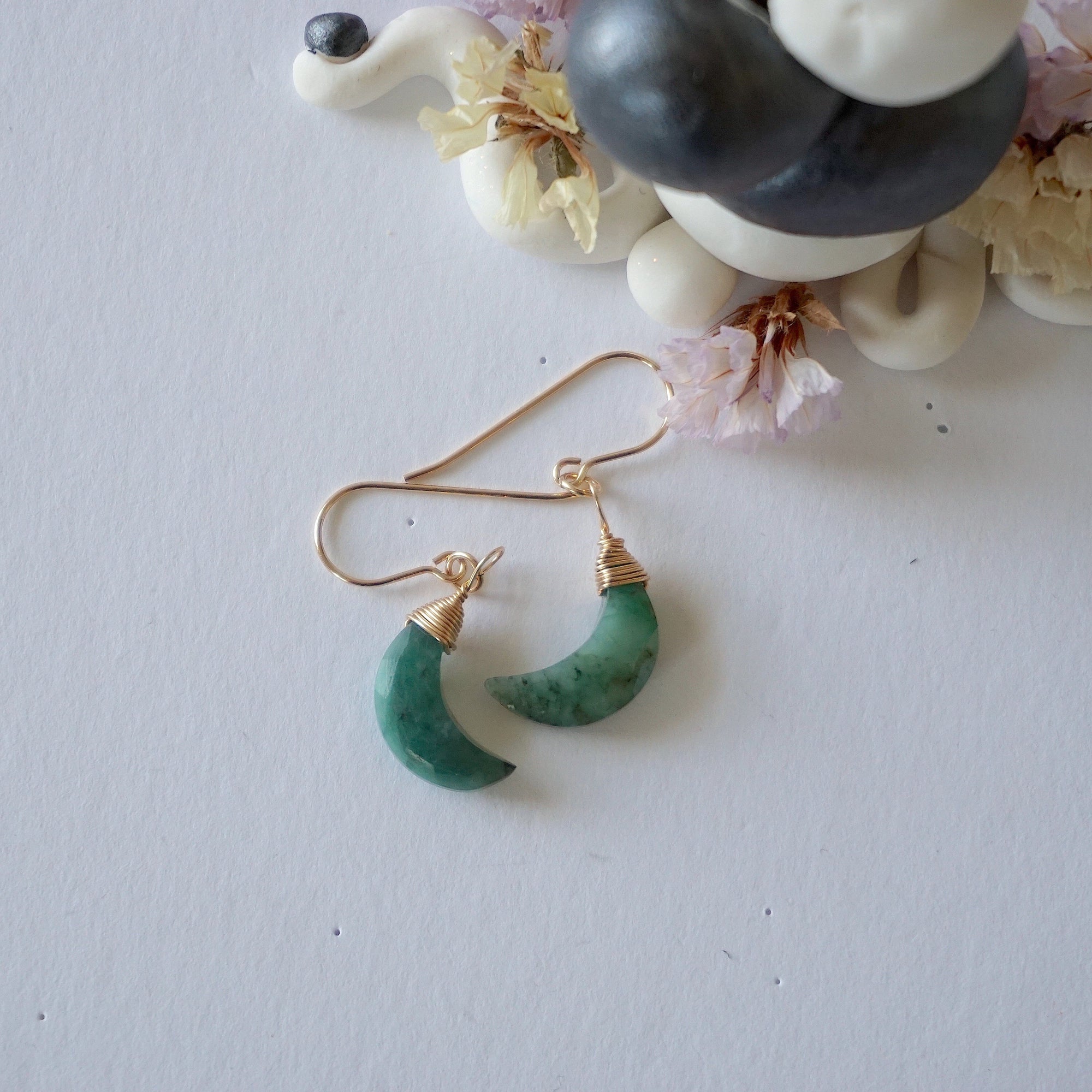 Emerald moon drop earrings in 14k gold filled displayed on a flat surface with natural faceted crescent moon emeralds.