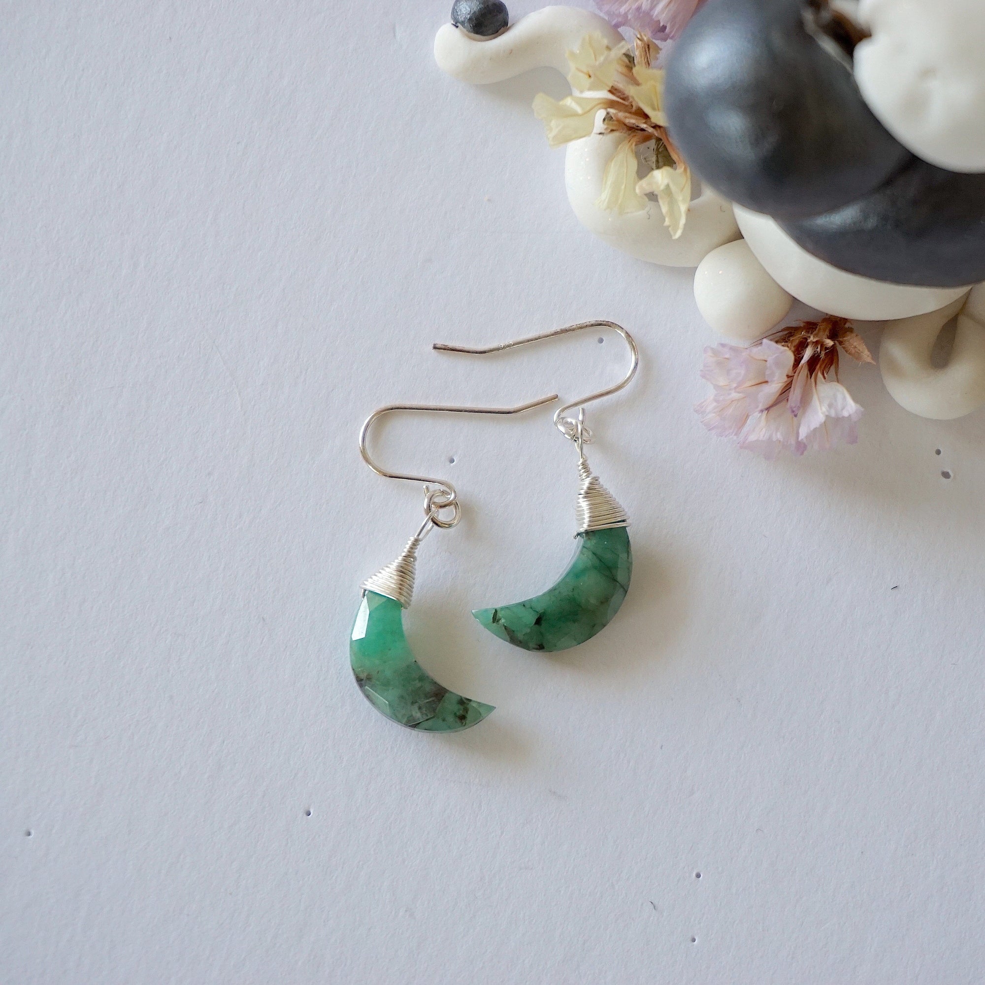 Emerald moon drop earrings in 925 sterling silver displayed on a flat surface with natural faceted crescent moon emeralds.