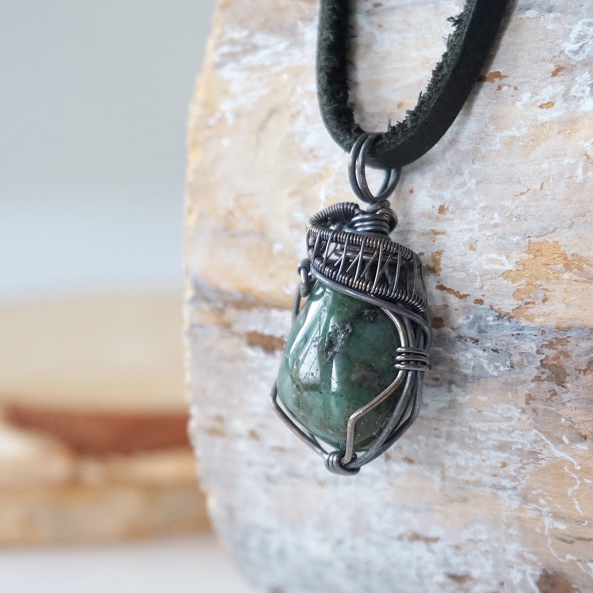 Left angle detail of emerald pendant for men showing natural polished-raw emerald and artisan antiqued sterling silver wire wrapping