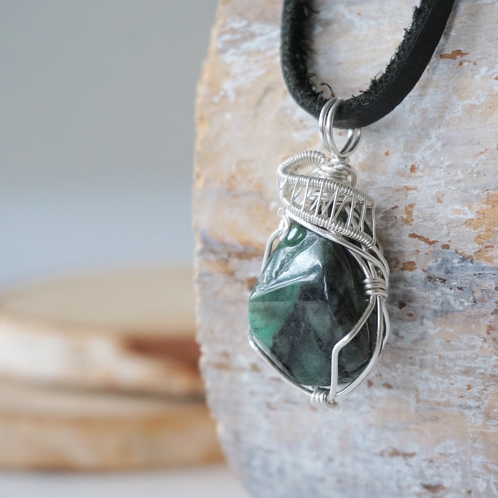 Left angle view of emerald pendant for men highlighting polished-raw emerald and artisan sterling silver wrapping.