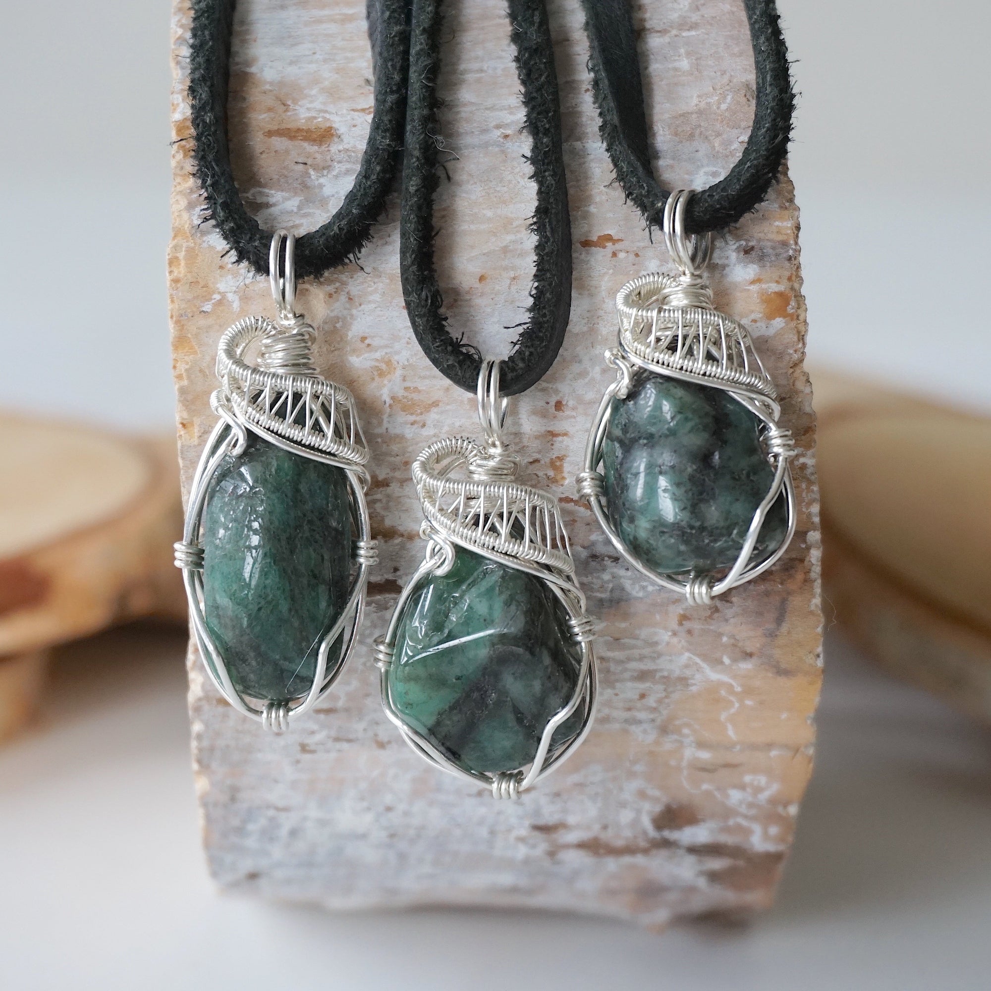 Three emerald pendants for men showing natural variation in size, shape, and green colour with sterling silver wire wrapping.