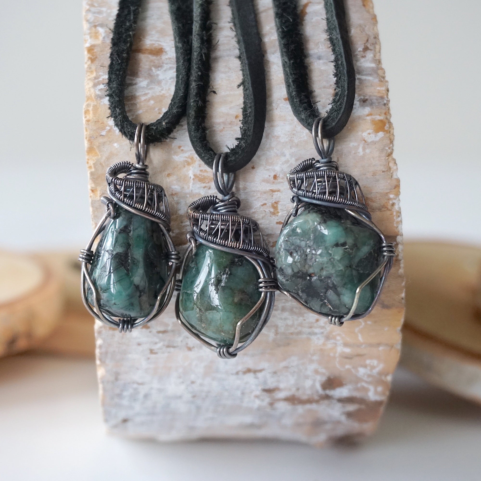 Three emerald pendants for men showing natural variation in emerald size, shape, and green colour in antiqued sterling silver wrapping
