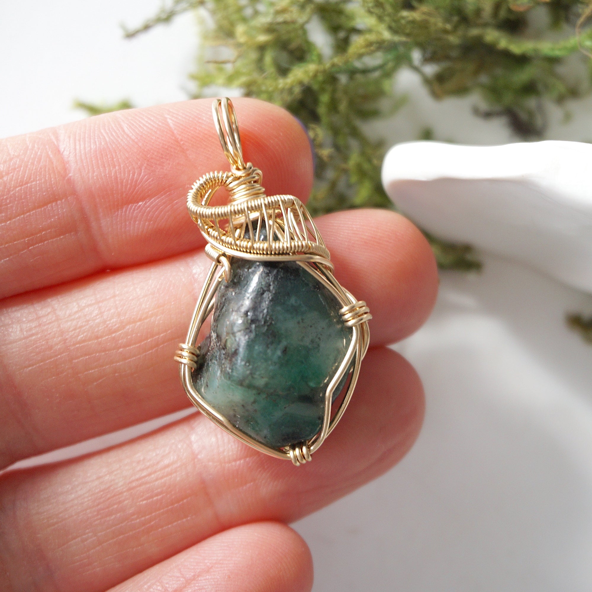 Natural raw emerald pendant shown in hand for size reference, wrapped in detailed 14k gold-filled wire.