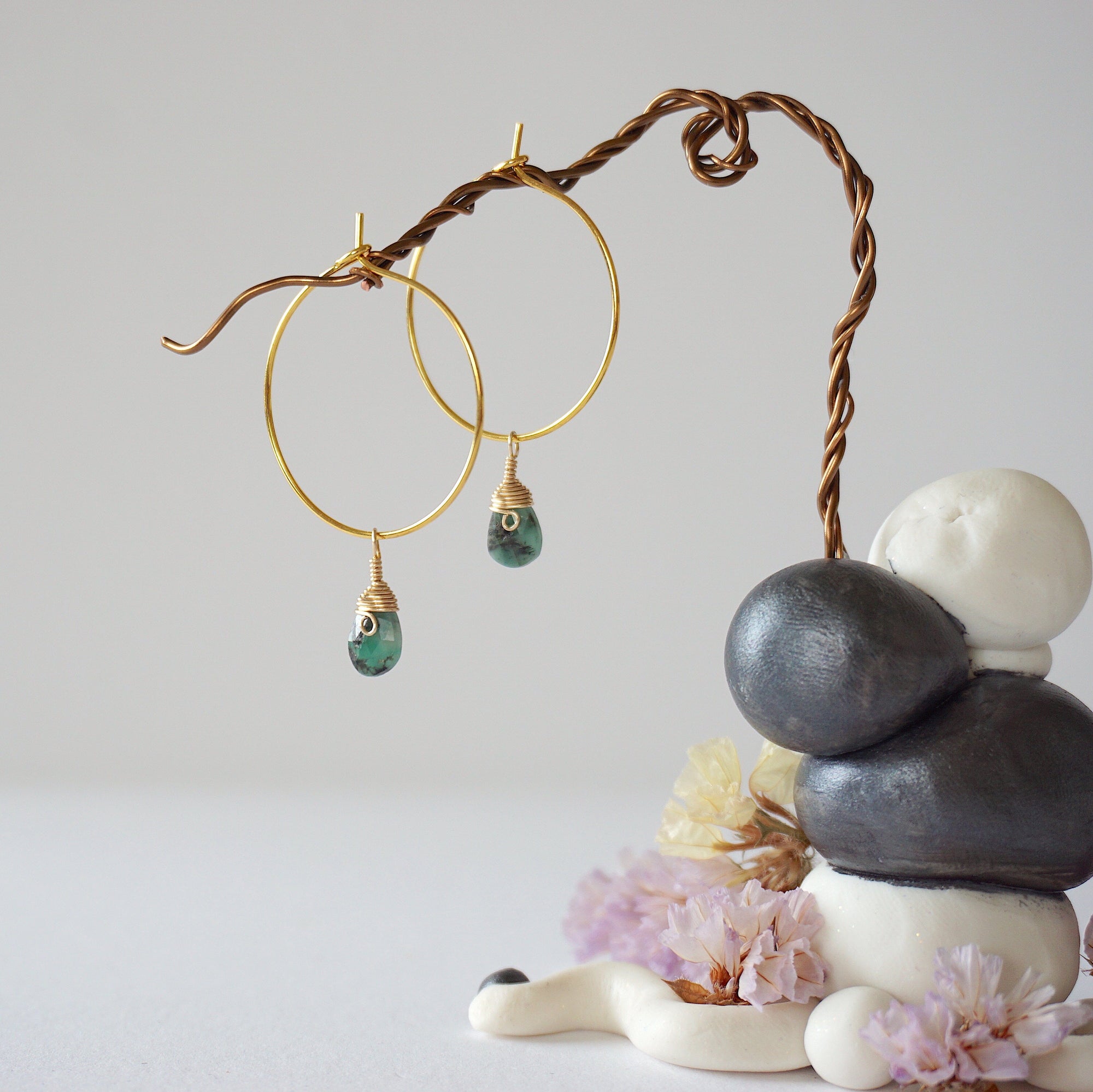 Angled close detail of faceted emerald hoop drop earrings showing artisan wire wrapping in warm gold copper